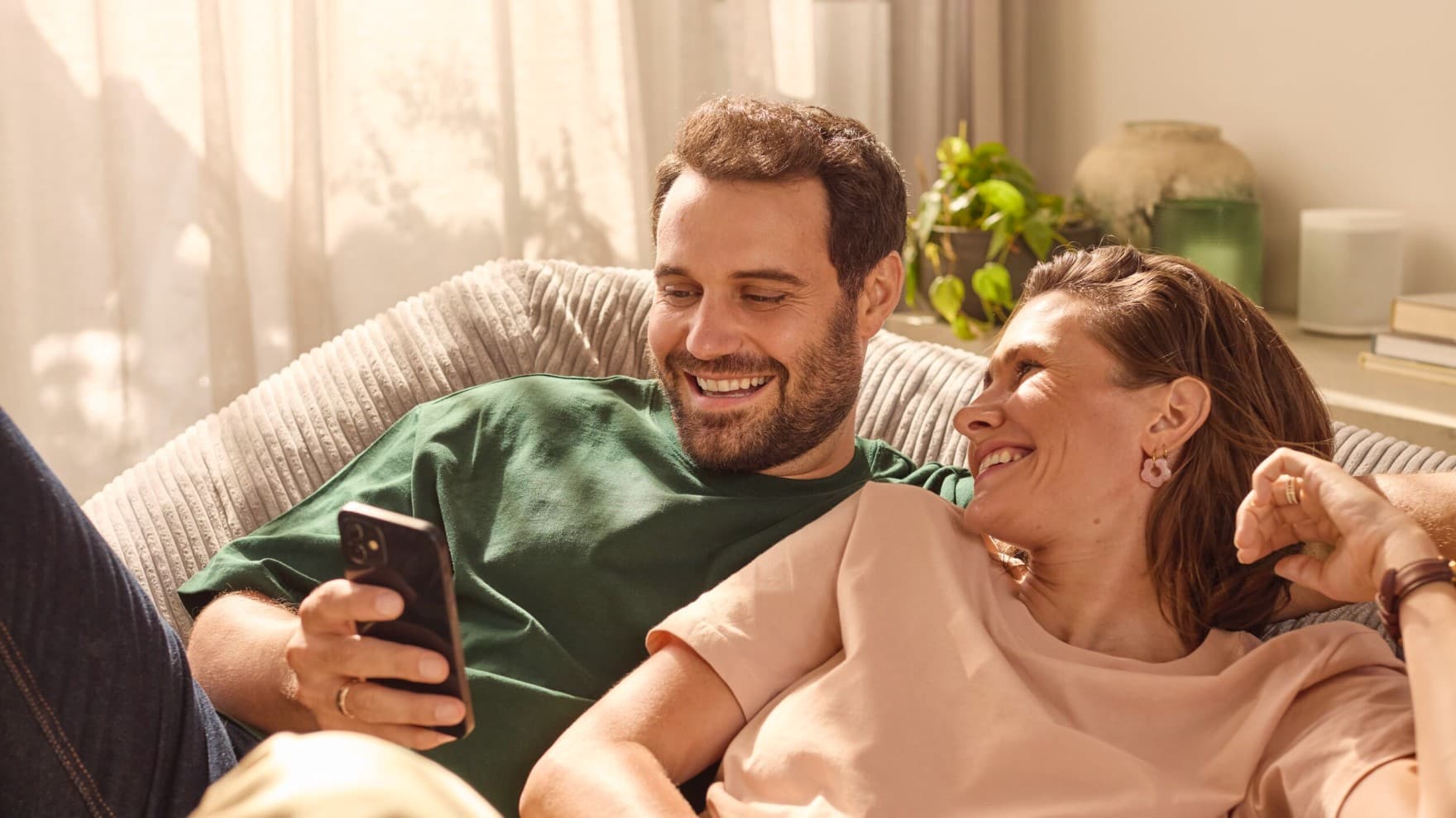 Ein Mann und eine Frau liegen auf einem Sofa und schauen gemeinsam auf ein Smartphone
