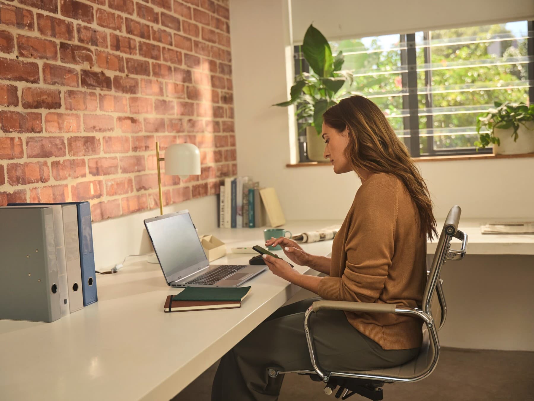 Frau sitzt mit Handy im Büro vor Laptop