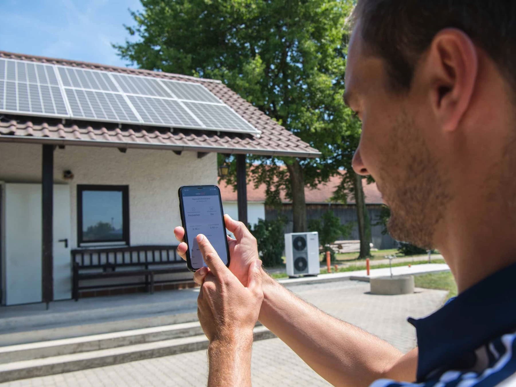 Mann vor einem Haus, der seine PV Anlage mit dem Smartphone abliest.