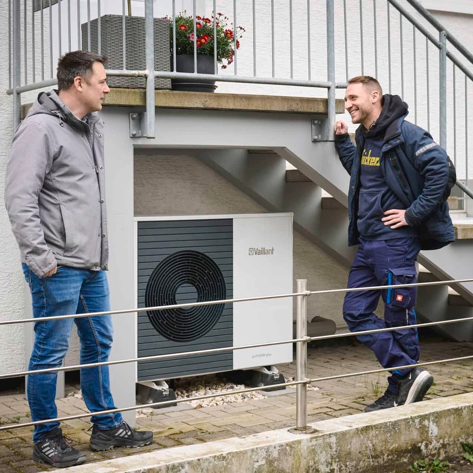 Hausbesitzer und Fachhandwerker unterhalten sich vor der Wärmepumpen Außeneinheit