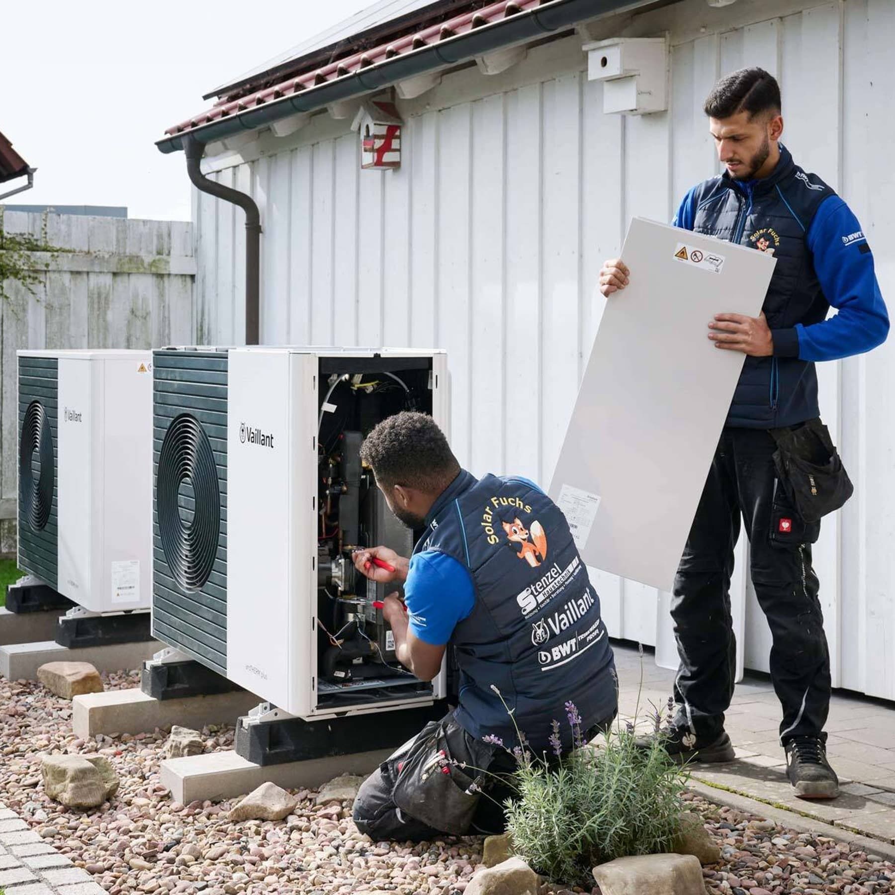 Zwei Handwerker installieren eine Wärmepumpen Außeneinheit
