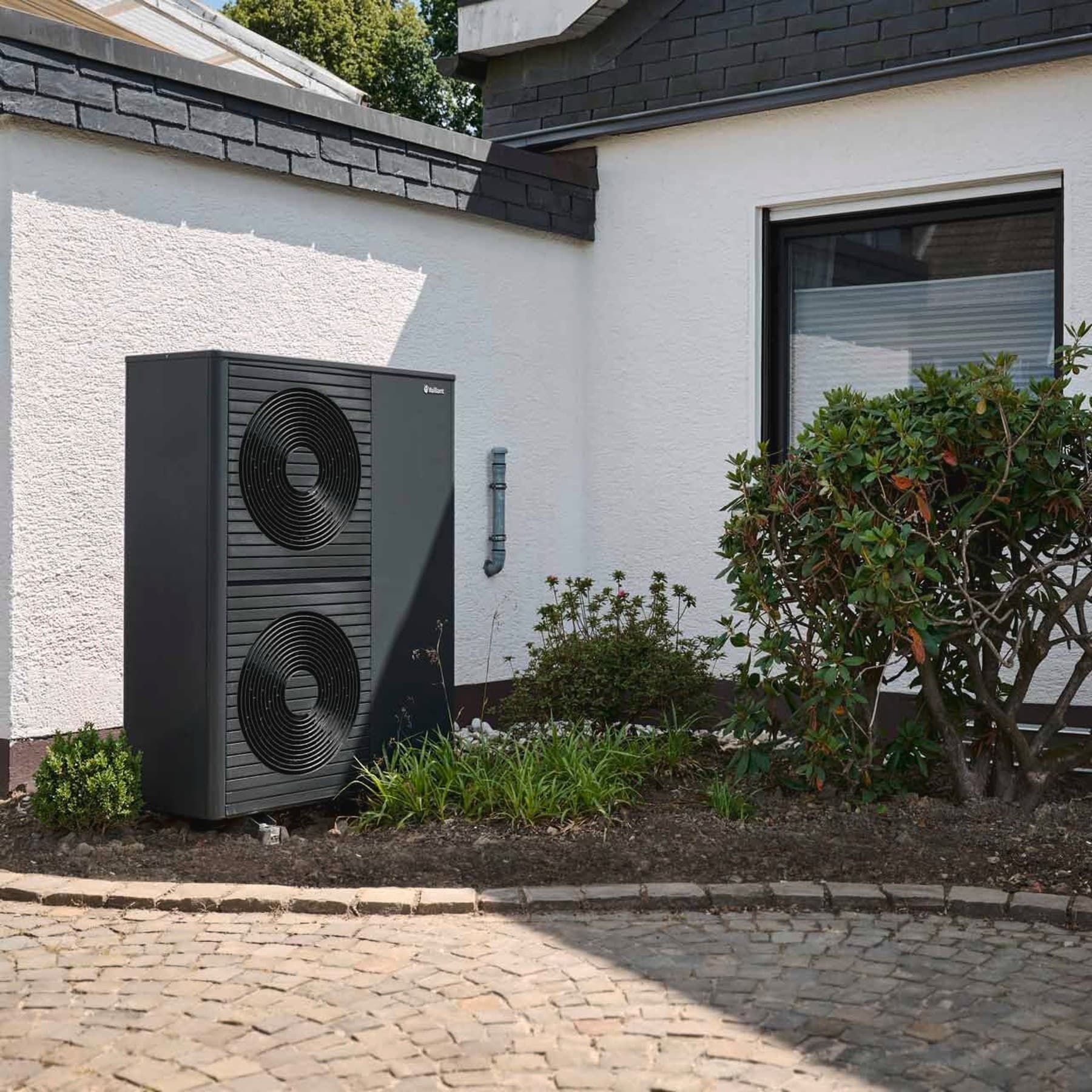 Doppelstöckige Wärmepumpe aroTHERM plus im Vorgarten vor weißer Hauswand