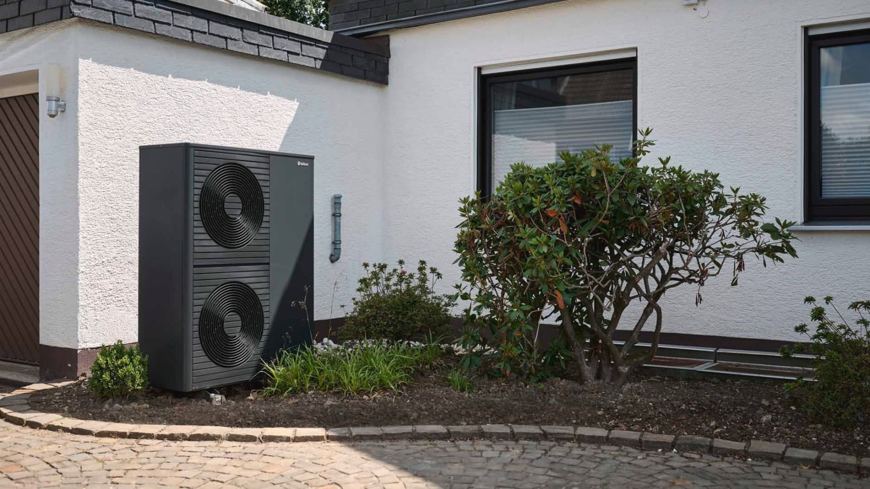 Doppelstöckige Wärmepumpe im Vorgarten vor einer weißen Hauswand