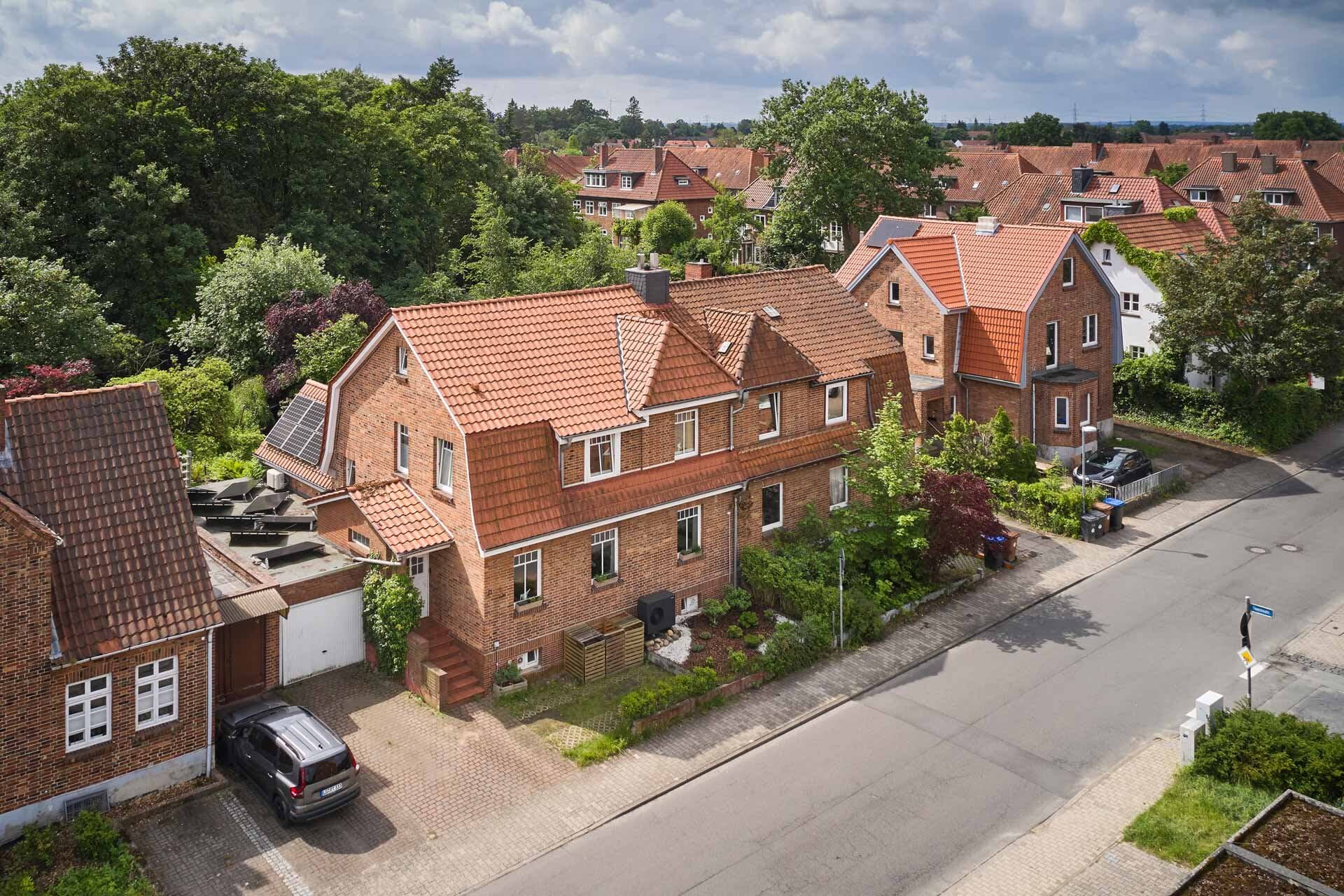 Luftaufnahme eines Backstein-Doppelhauses in einer Wohnstraße mit roten Ziegeldächern und sichtbarer Außeneinheit der Luft-Wasser-Wärmepumpe aroTHERM plus VWL 75/8.1 A von Vaillant an der Fassade.