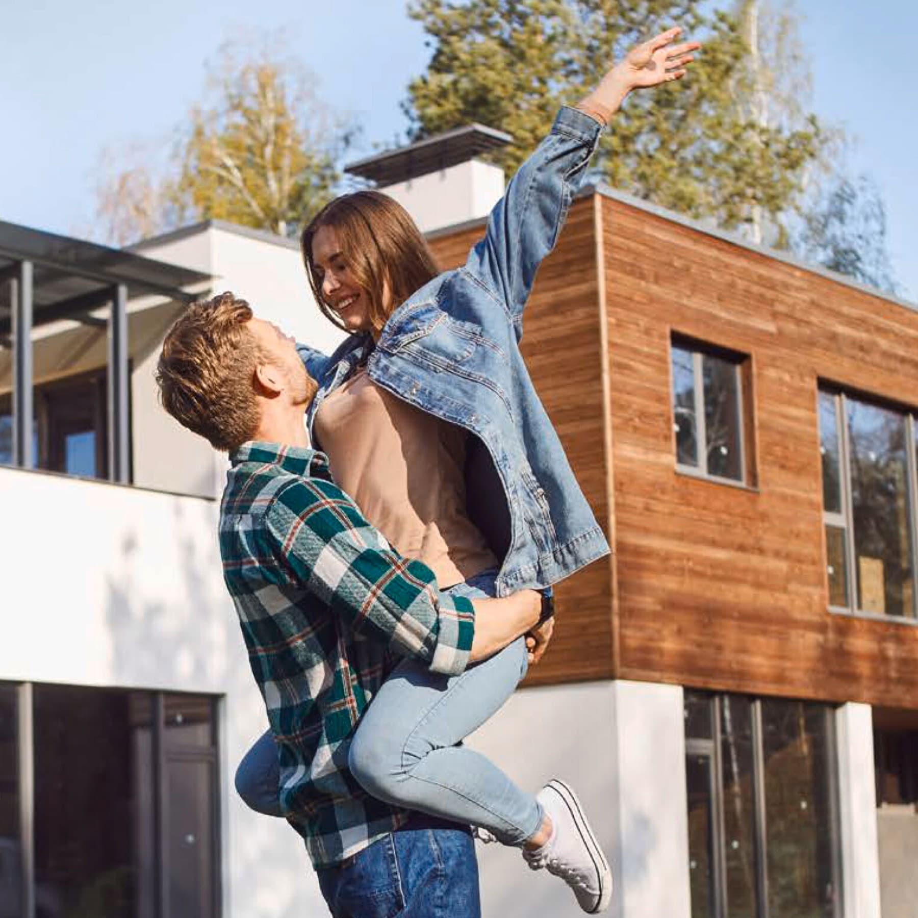Ein Mann hebt eine Frau vor einem Neubau hoch.
