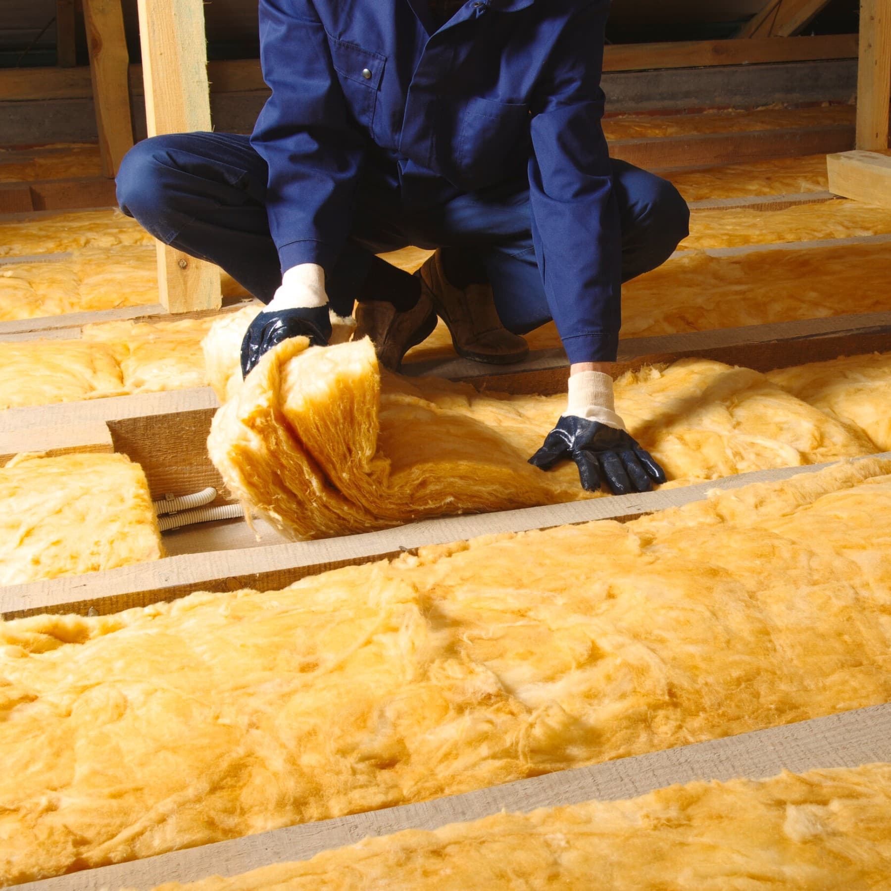 Ein Mann verlegt hockend Dämmwolle auf einem Fußboden