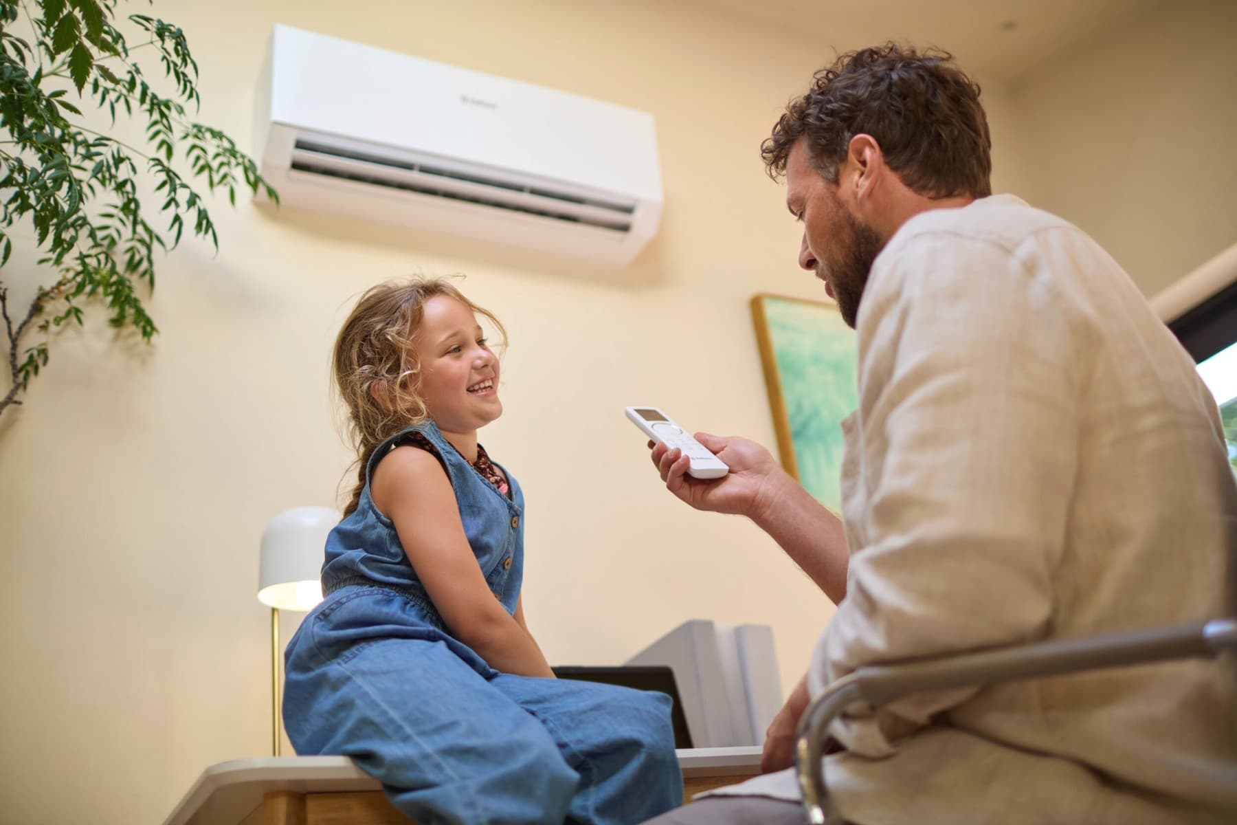 Ein Mann sitzt mit Fernbedienung in der Hand vor einem lächelnden Mädchen. Im Hintergrund hängt eine Vaillant Klimaanlage an der Wand.