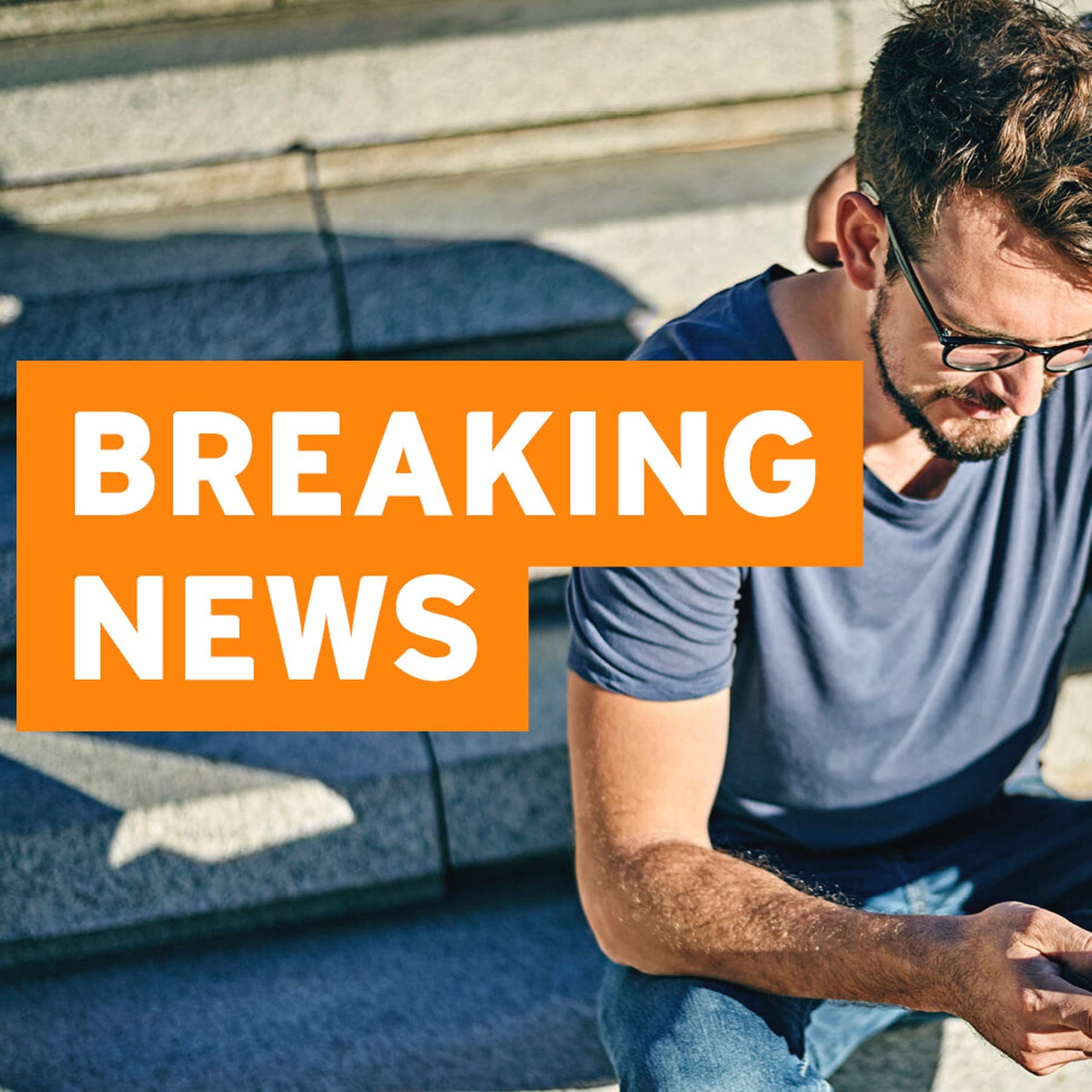 Bild zeigt zwei Männer, die auf sonnenbeschienener Treppe sitzen und gemeinsam auf ein Smartphone gucken, im Vordergrund befindet sich ein oranger Balken mit der weißen Aufschrift: breaking news