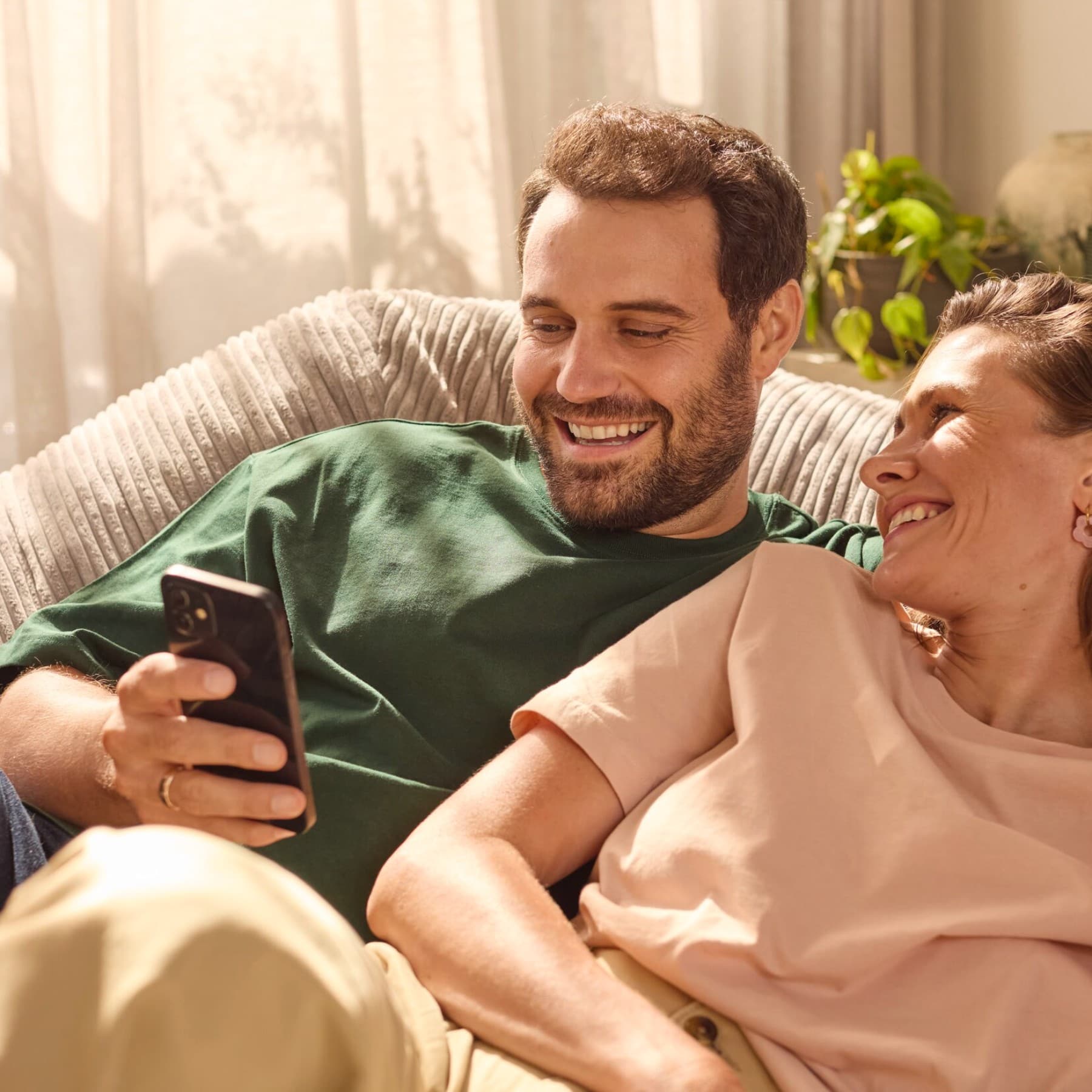 Eine Frau und ein Mann sitzen gemeinsam auf einer Couch und schauen auf ein Smartphone.