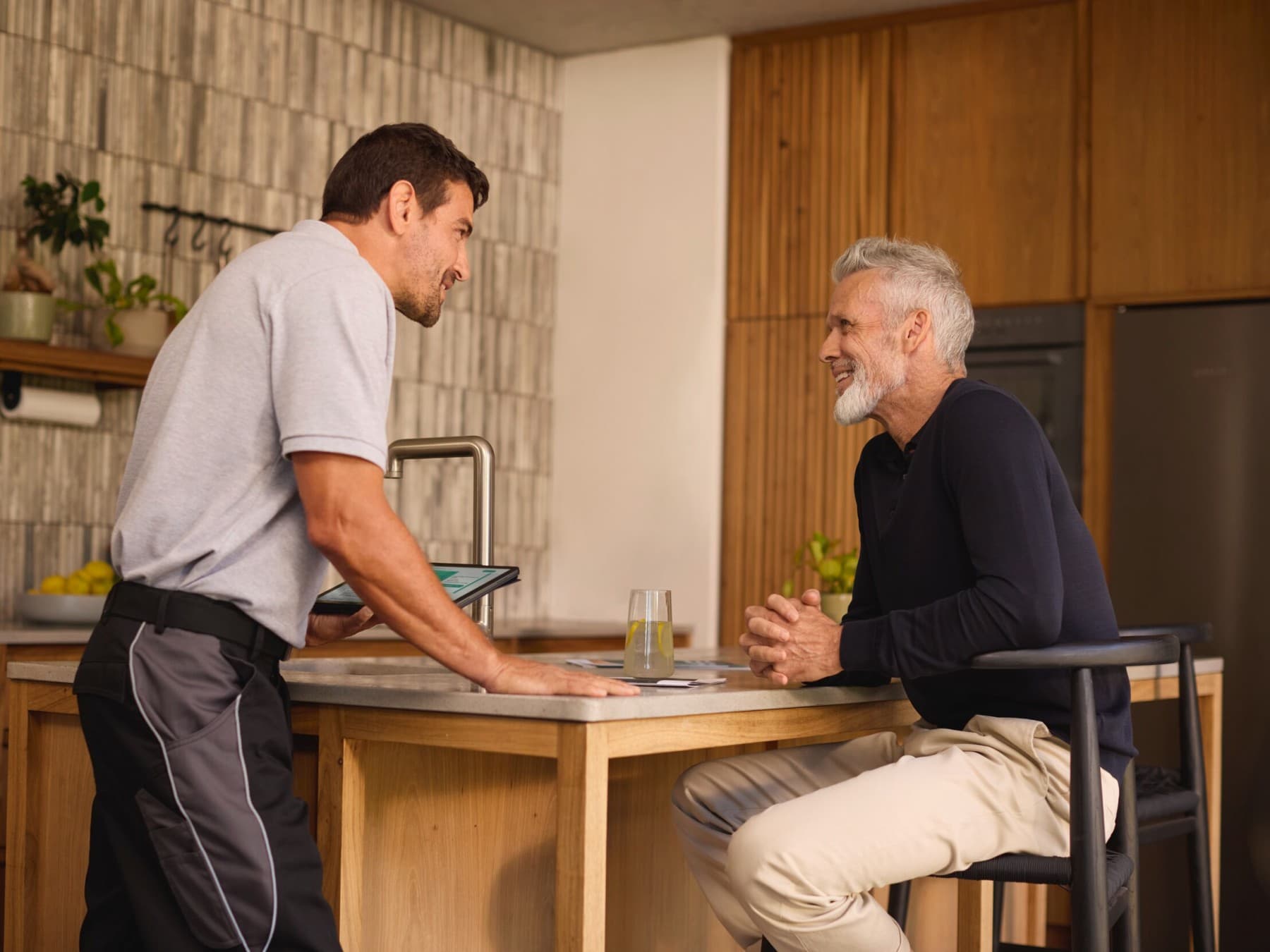 Ein Fachhandwerker hält ein Tablet in seiner linken Hand und berät einen Kunden, beide befinden sich in einer Küche