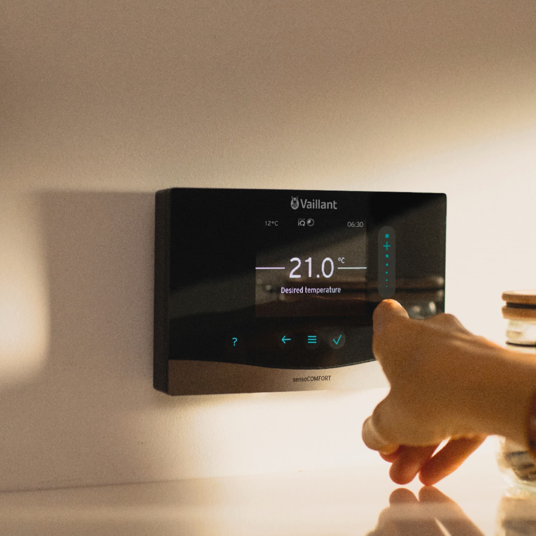 Eine Hand bedient einen digitalen Vaillant Regler, der an einer Wand hängt.