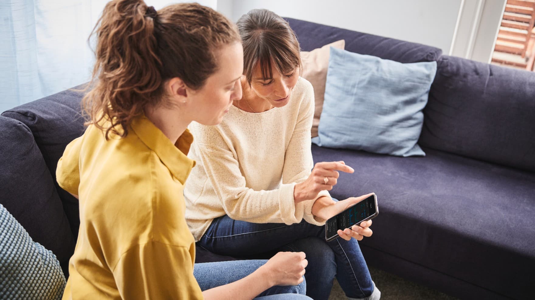 Zwei Frauen, die gemeinsam auf ein Smartphone gucken.