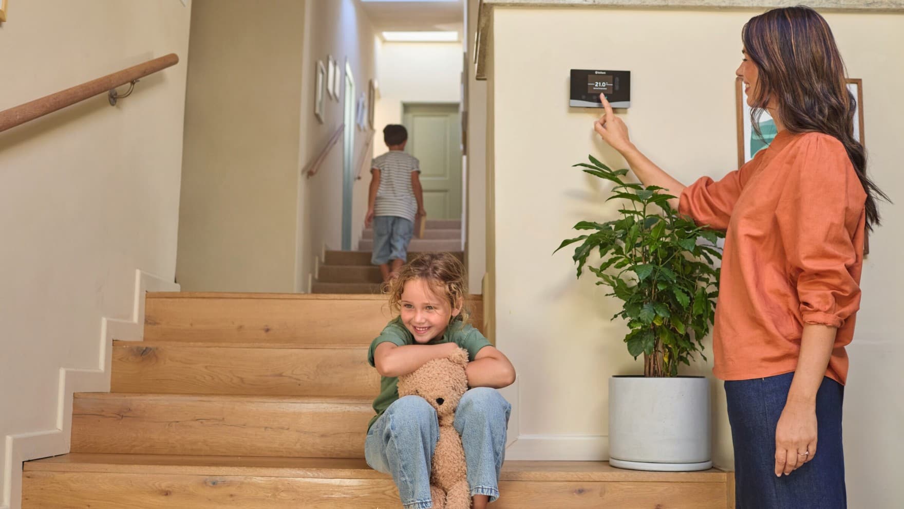 Frau, die einen Vaillant Regler bedient. Auf der Treppe sind zwei Kinder zu sehen.