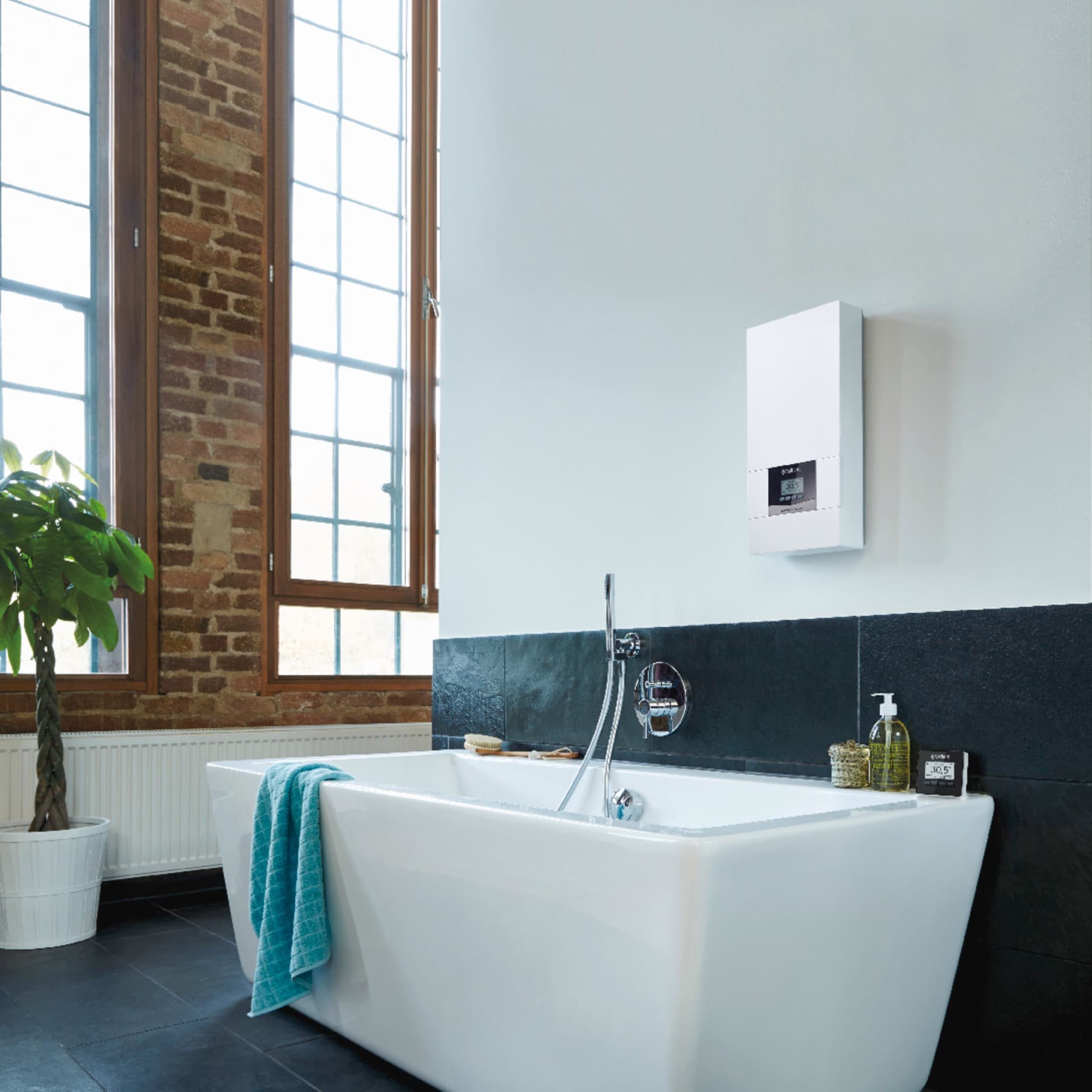 Ein Vaillant Durchlauferhitzer hängt in einem Bad über einem schwarzen Fliesenspiegel über einer Badewanne.