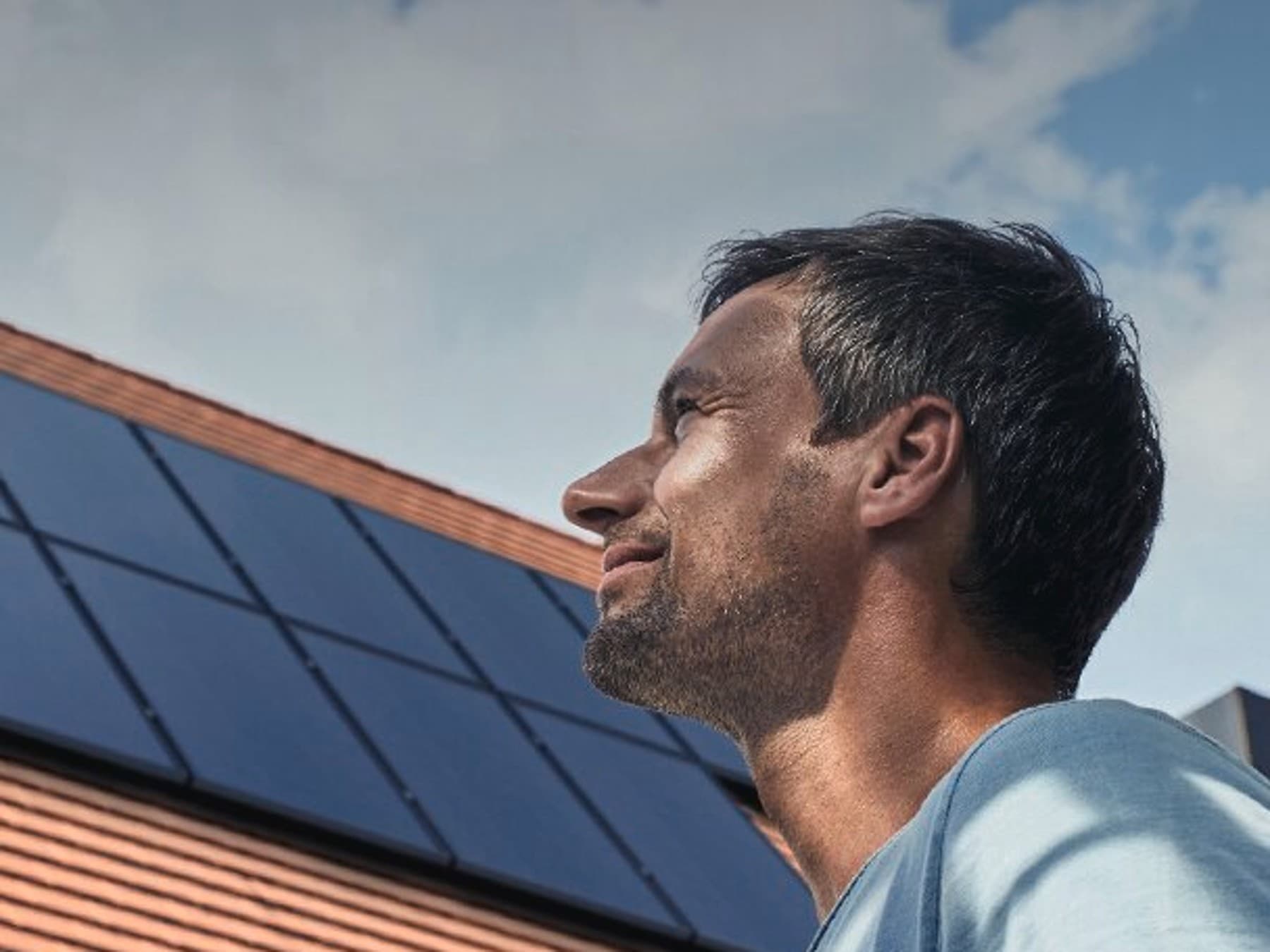 Ein Mann steht vor einem Haus mit Solarpaneelen. Im Hintergrund ist das Dach mit der Solaranlage zu sehen.