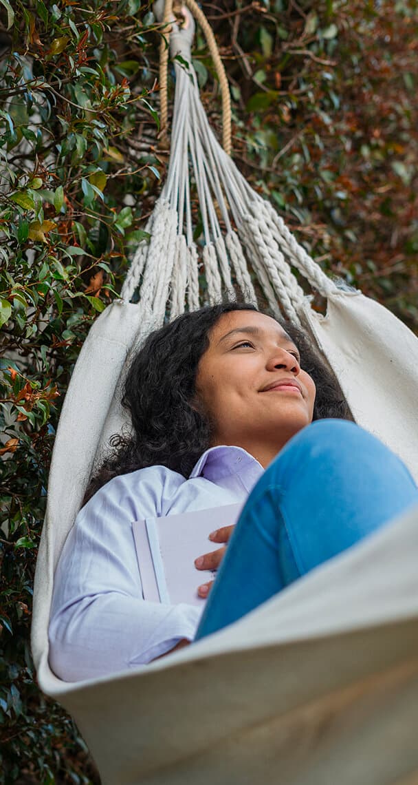 Eine Frau liegt mit einem Notizbuch in der Hand in einer Hängematte.