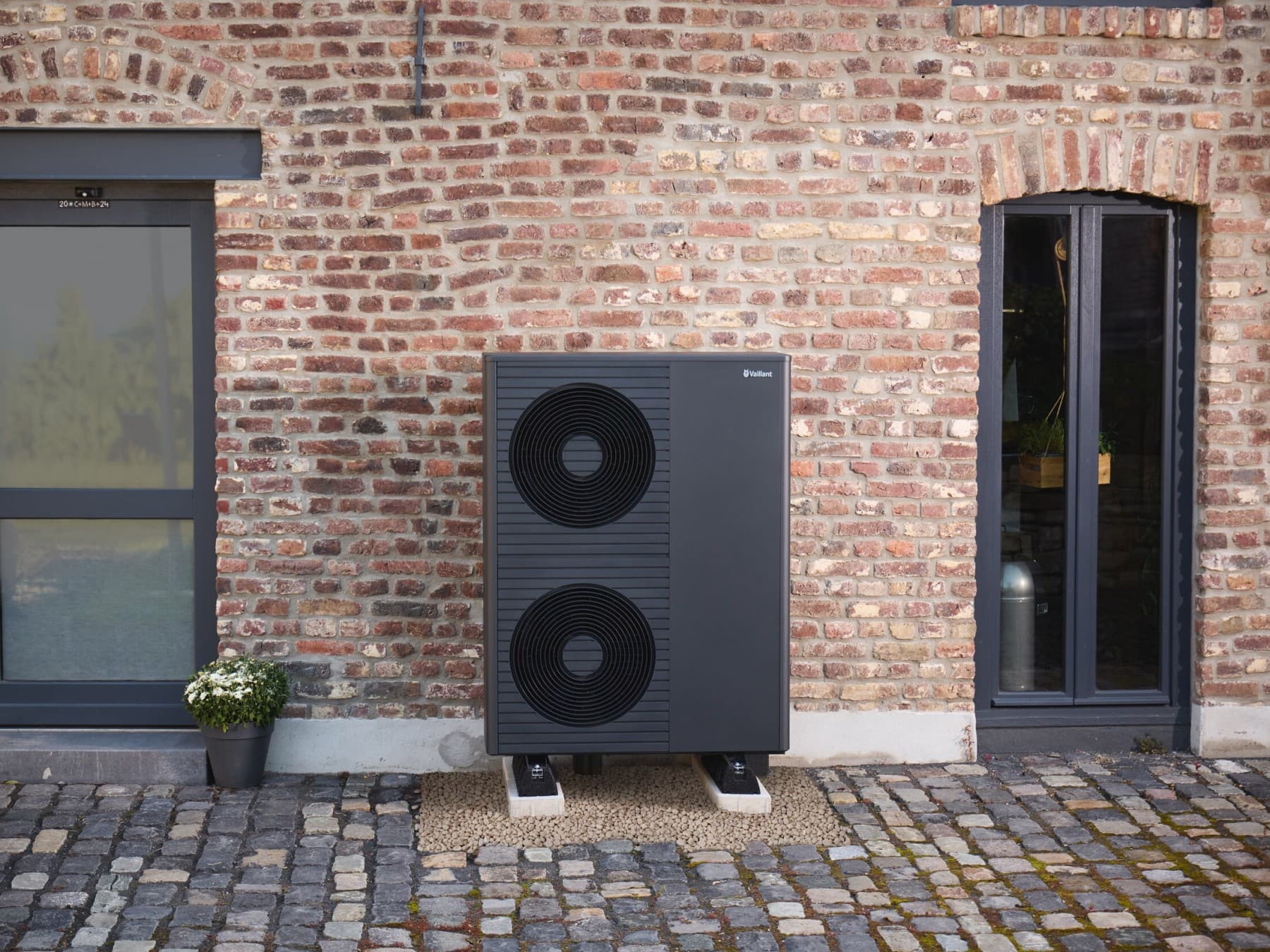 Außeneinheit der Luft-Wasser-Wärmepumpe aroTHERM plus von Vaillant als Doppellüfter vor einem Backsteinhaus
