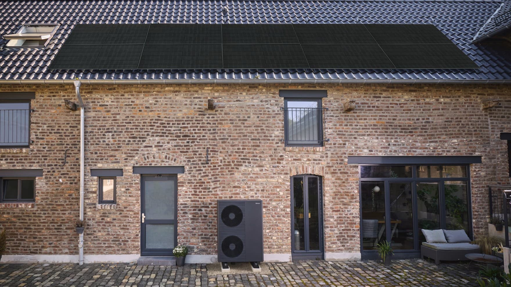 Vaillant Wärmepumpe in elegantem Design vor einer Hauswand und einer Photovoltaikanlage auf dem Dach.