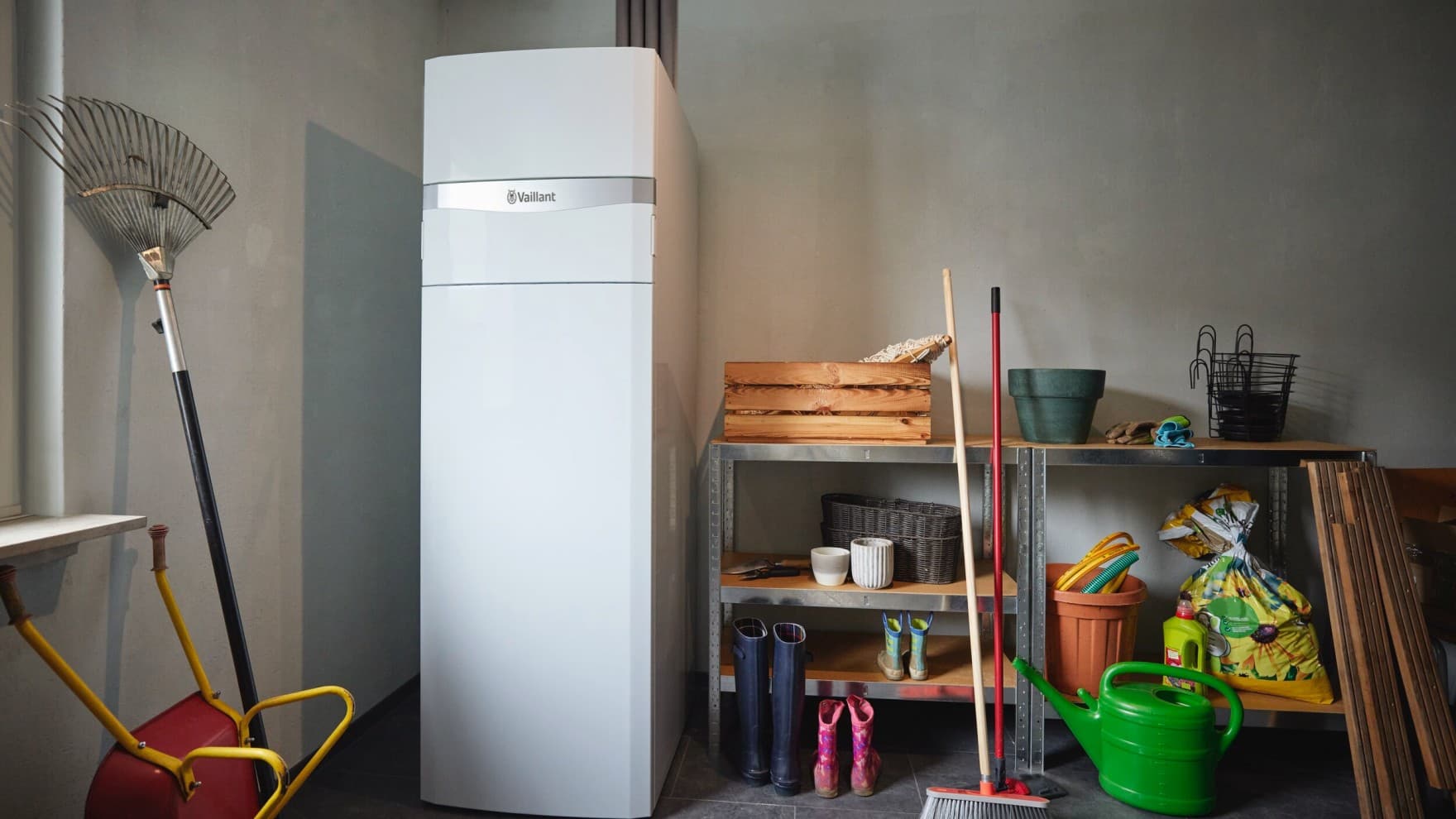 Die Vaillant Erdwärmepumpe flexoCOMPACT exclusive steht in einem Kellerraum neben Schwerlastregalen mit Gummistiefeln und anderem Zubehör für Gartenarbeit.