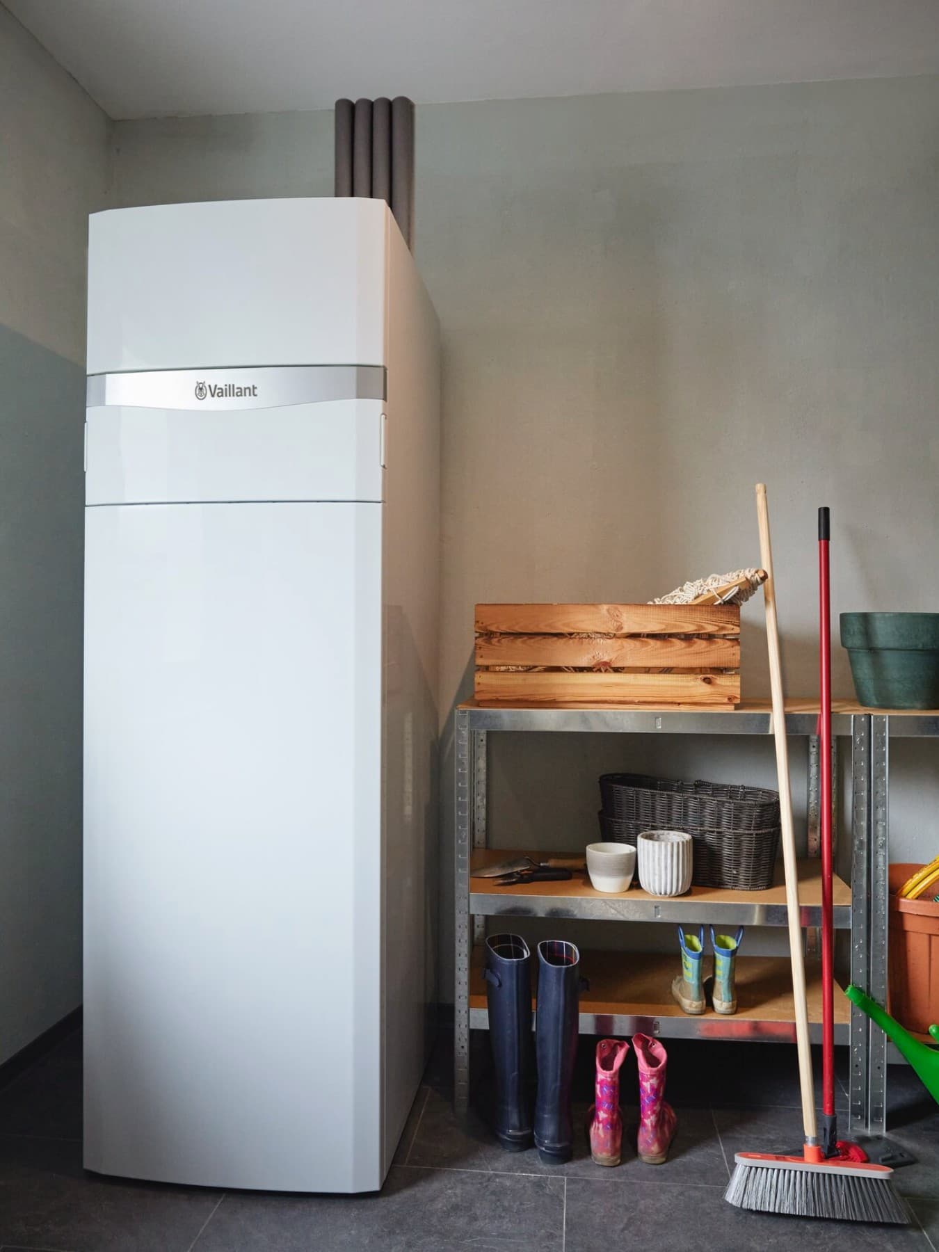 Die Vaillant Erdwärmepumpe flexoCOMPACT exclusive steht in einem Kellerraum neben Schwerlastregalen mit Gummistiefeln und anderem Zubehör für Gartenarbeit.