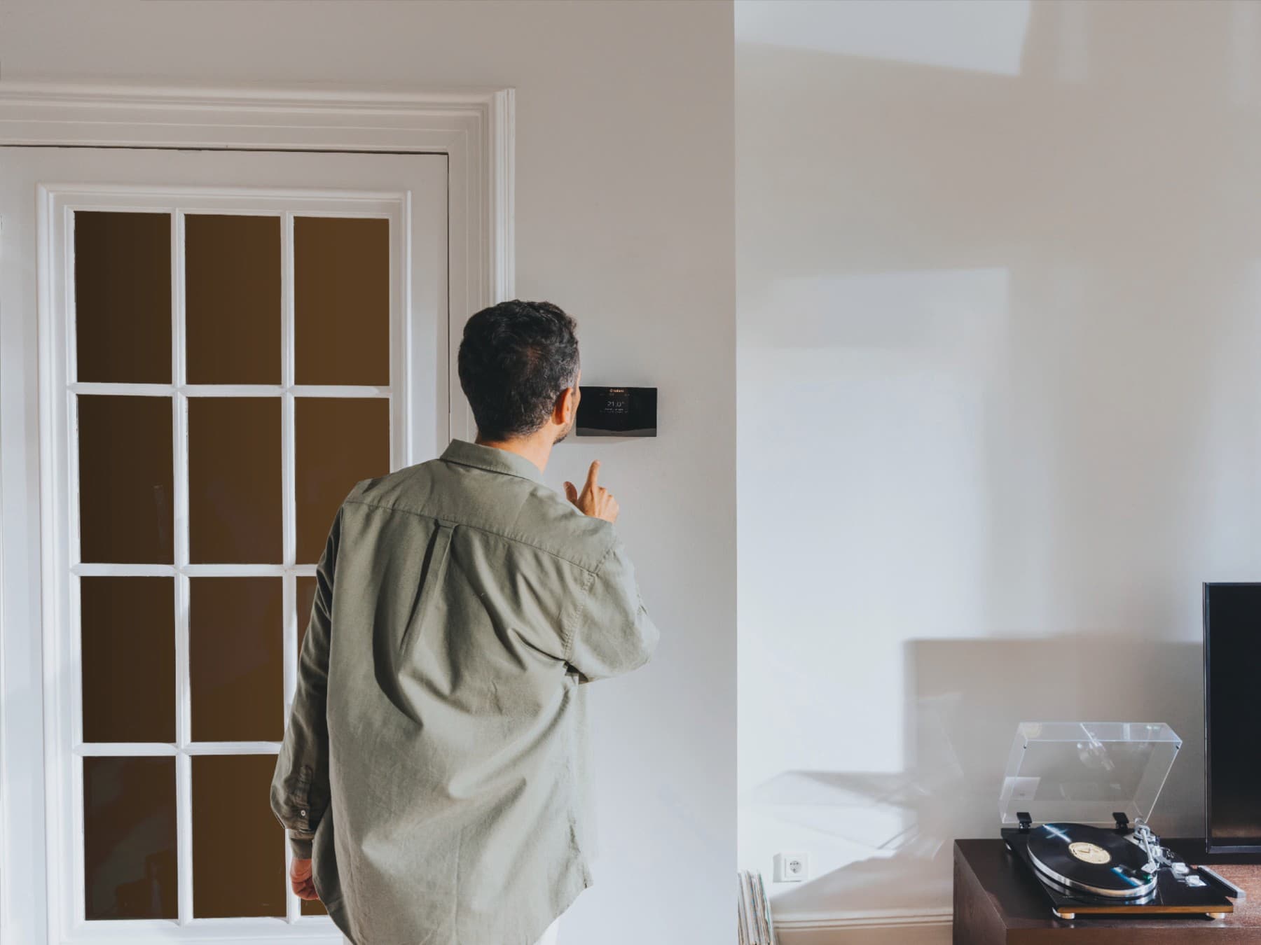 Mann schaut im Wohnzimmer auf den digitalen Regler seiner Heizung.