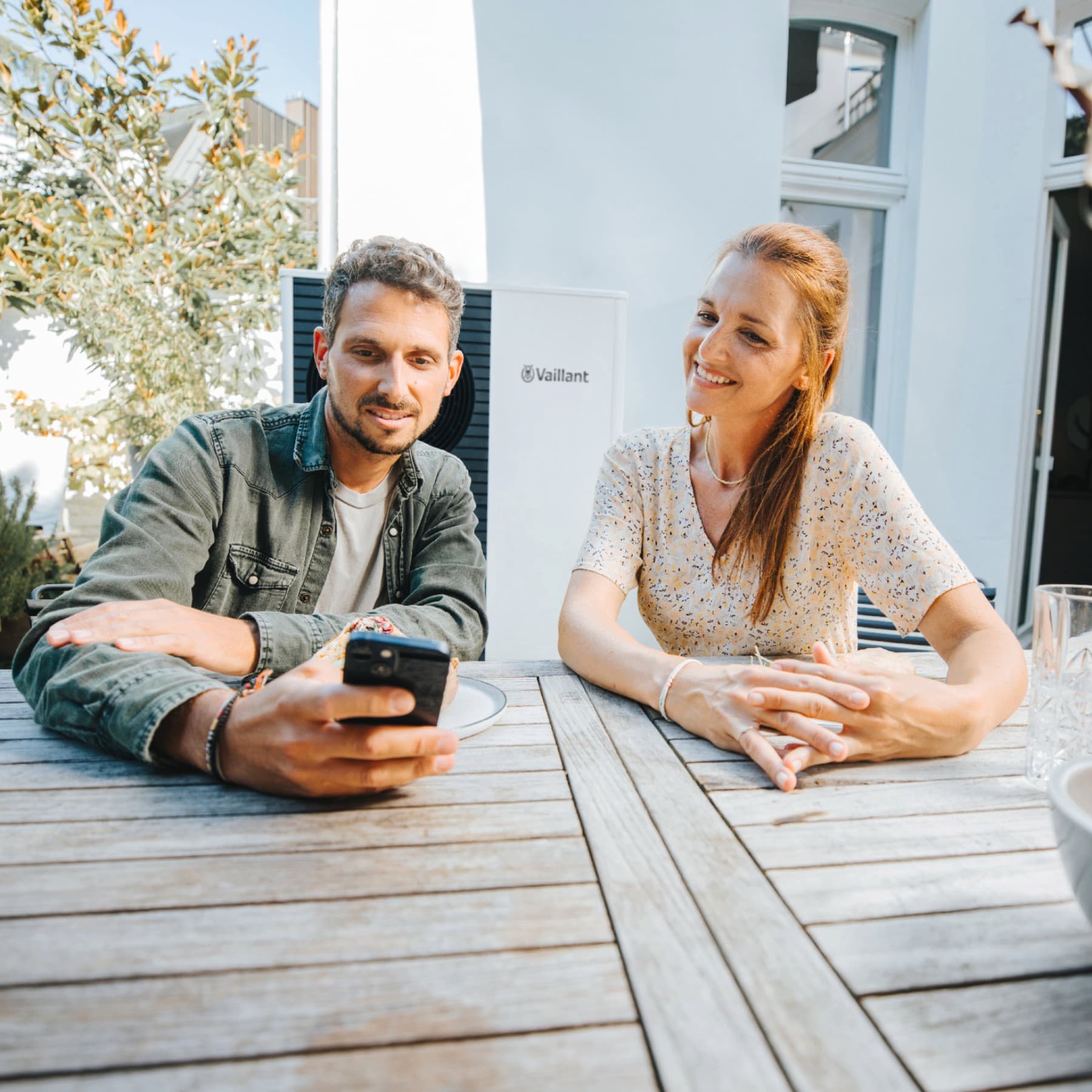 Ein Mann und eine Frau sitzen an einem Tisch und schauen auf ein Smartphone.