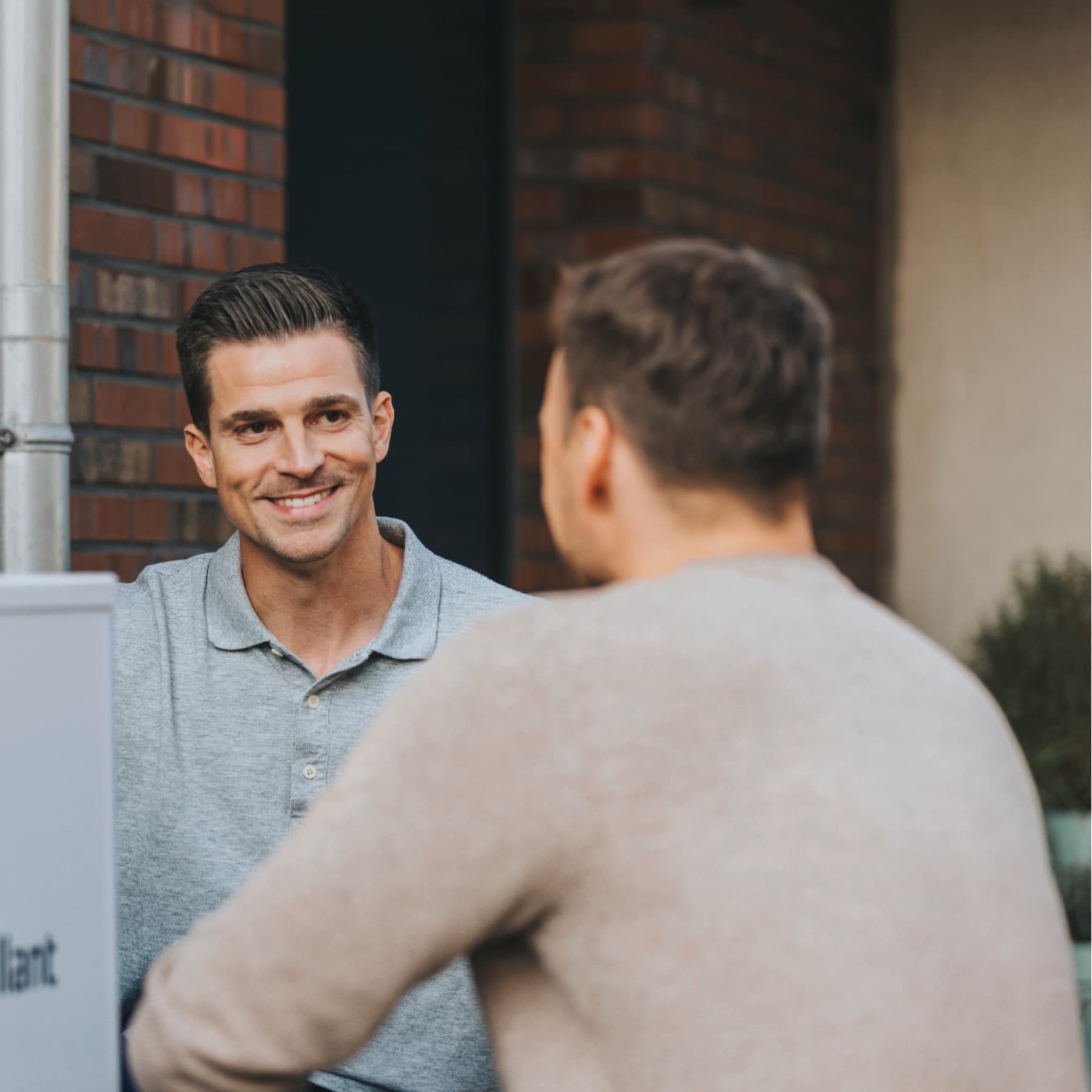 Ein Vaillant Fachhandwerker begrüßt einen Kunden, der neben einer Vaillant Wärmepumpe vor seinem Haus steht.
