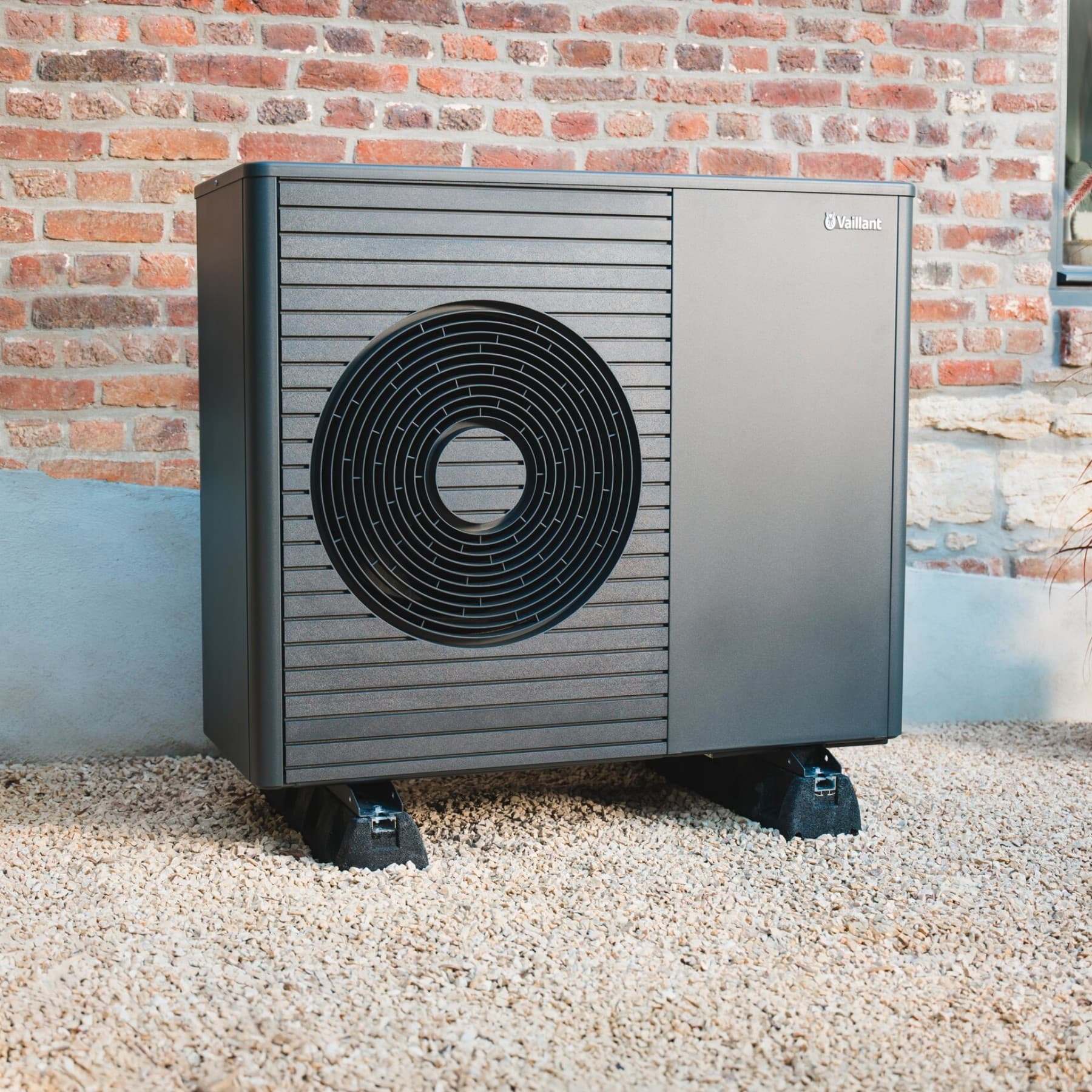 Eine Vaillant Wärmepumpe in schwarzgrau steht vor einem Backsteingebäude.