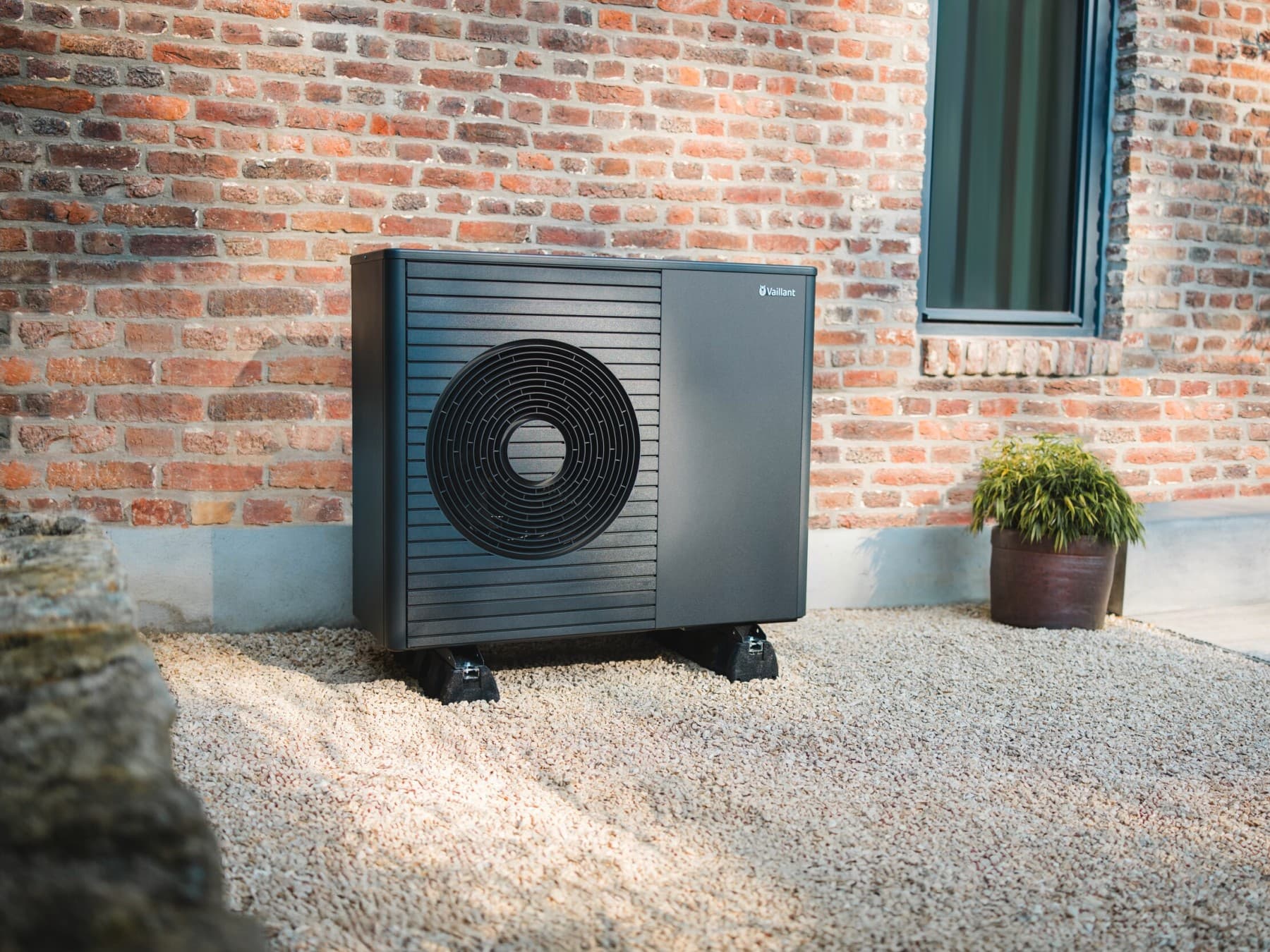 Eine Wärmepumpe steht vor einem Neubau, im Vordergrund sieht man einen gepflegten Rasen und einen Weg