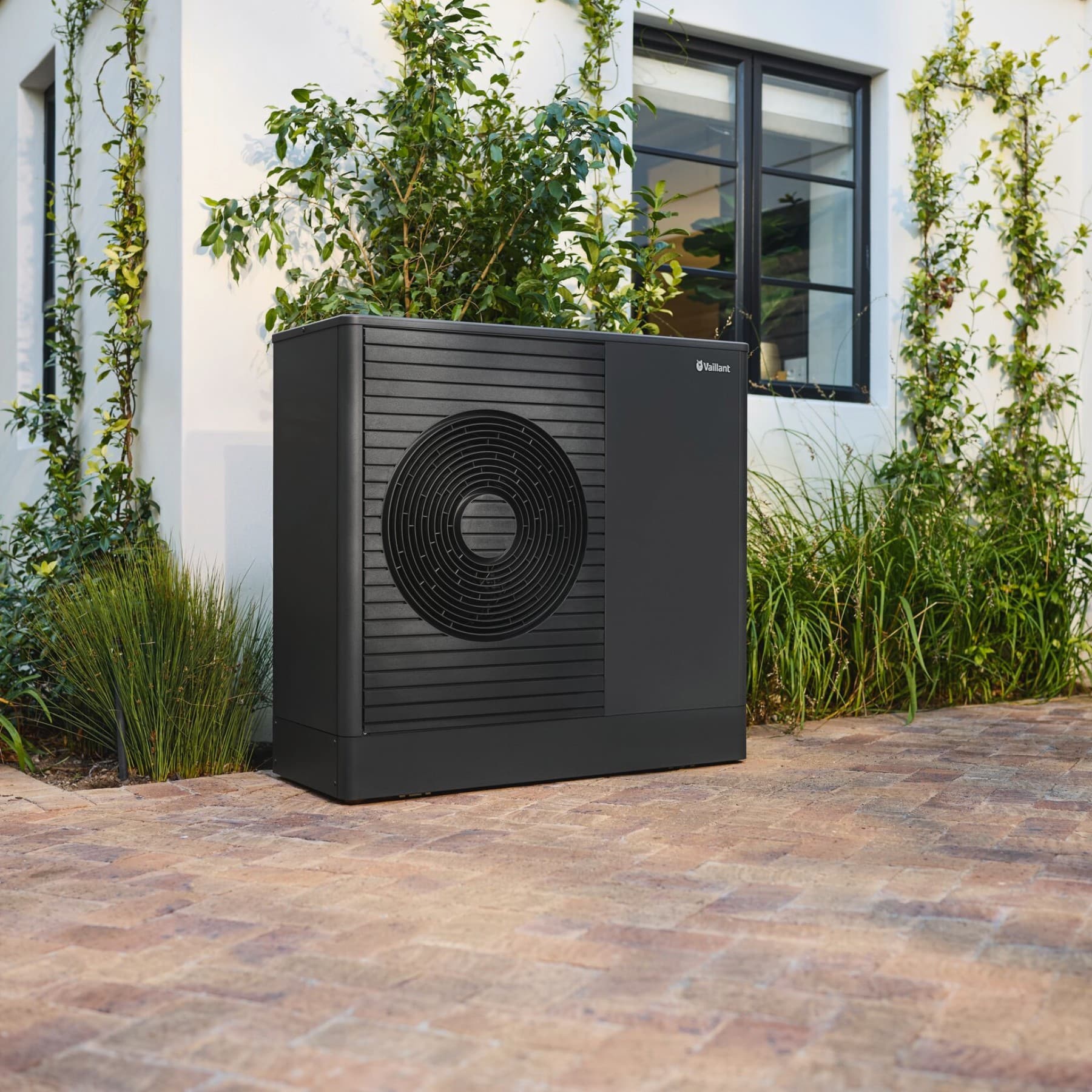 Eine schwarzgraue Wärmepumpe vom Typ aroTHERM plus steht vor einer Hauswand