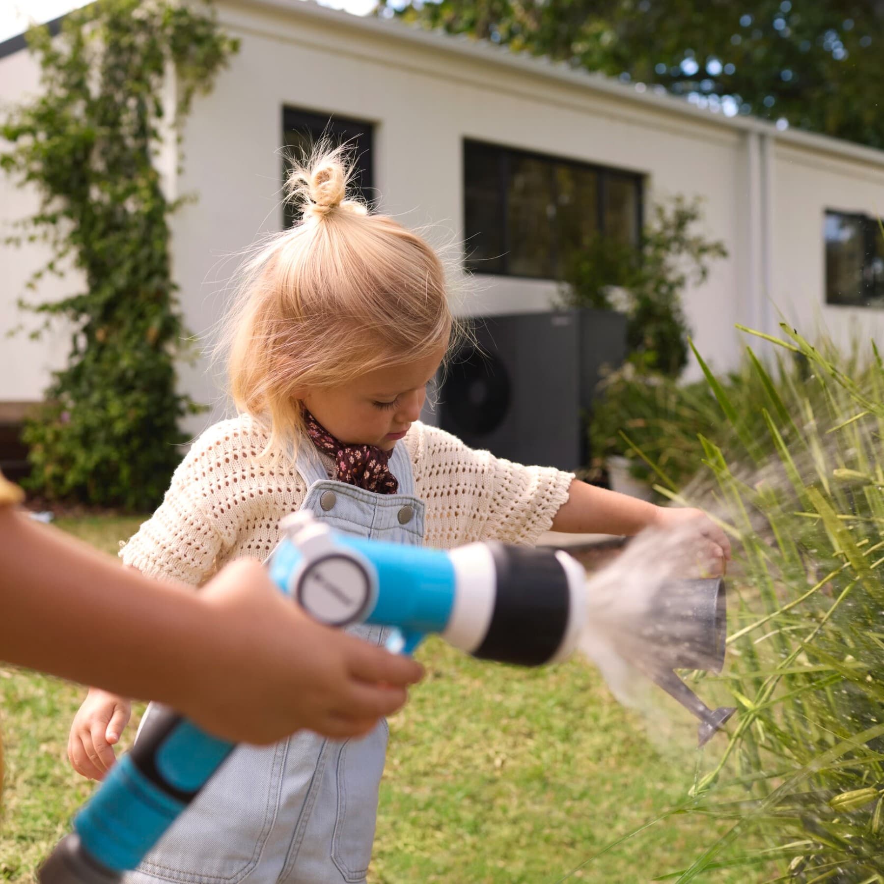Kinder, die in einem Garten Blumen mit einem Gartenschlauch bewässern.