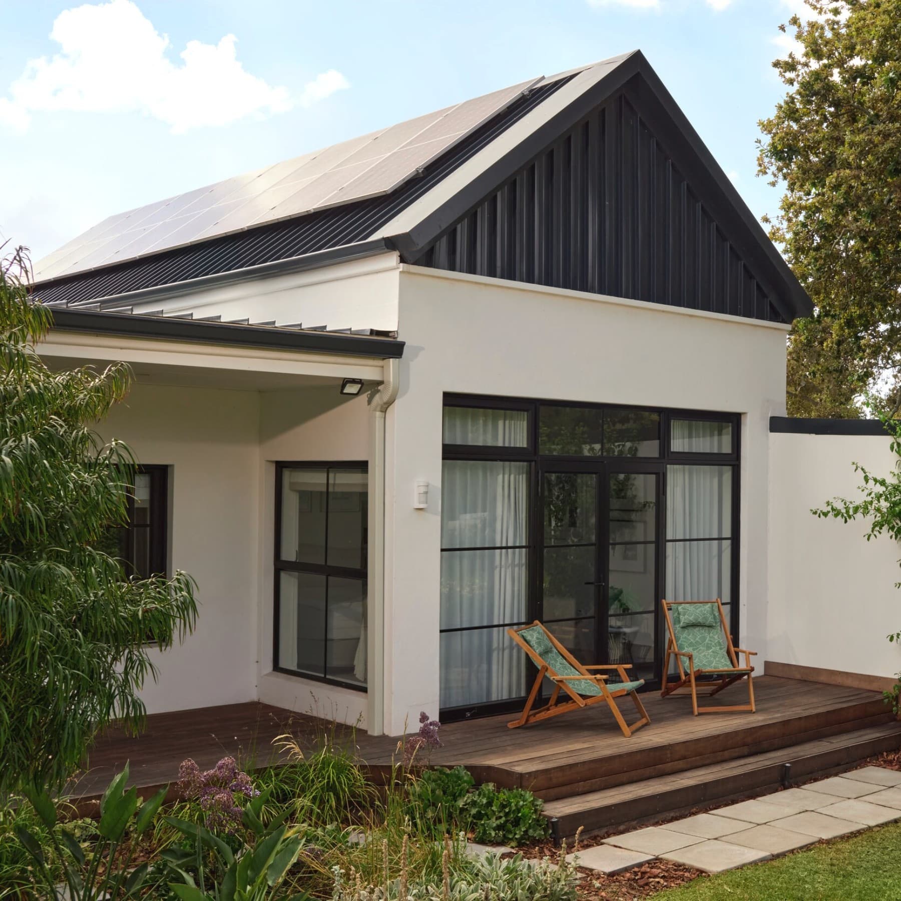 Ein modernes Haus vom Garten aus fotografiert. Auf dem Dach ist eine Photovoltaik-Anlage zu erkennen, rechts neben dem Haus steht eine Vaillant Wärmepumpe.