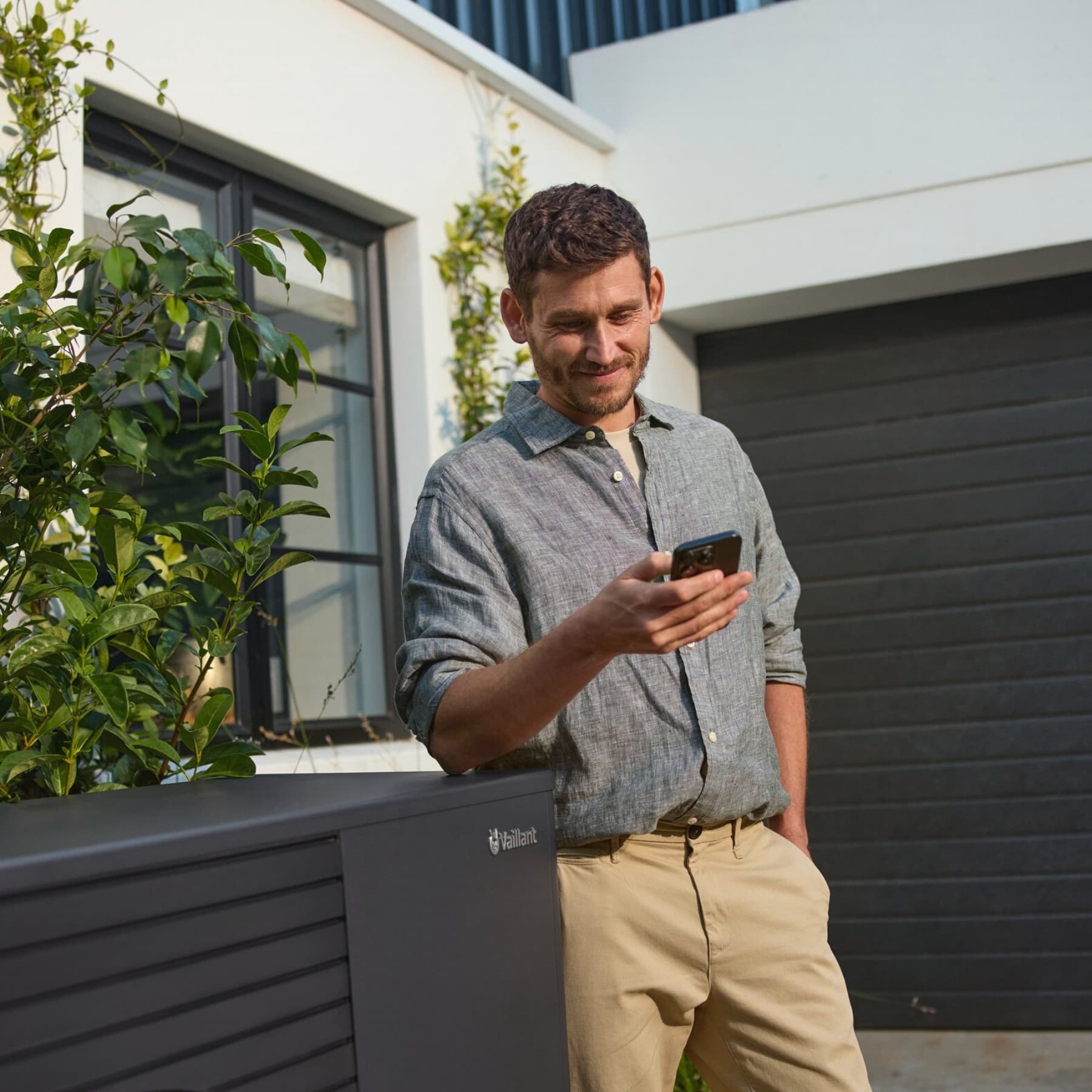 Mann steht mit Handy in der Hand neben einer Wärmepumpe.