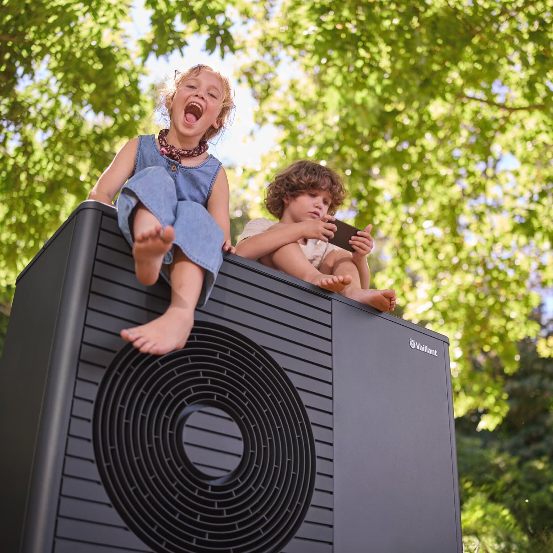 Zwei Kinder sitzen auf einer Vaillant Wärmepumpe.