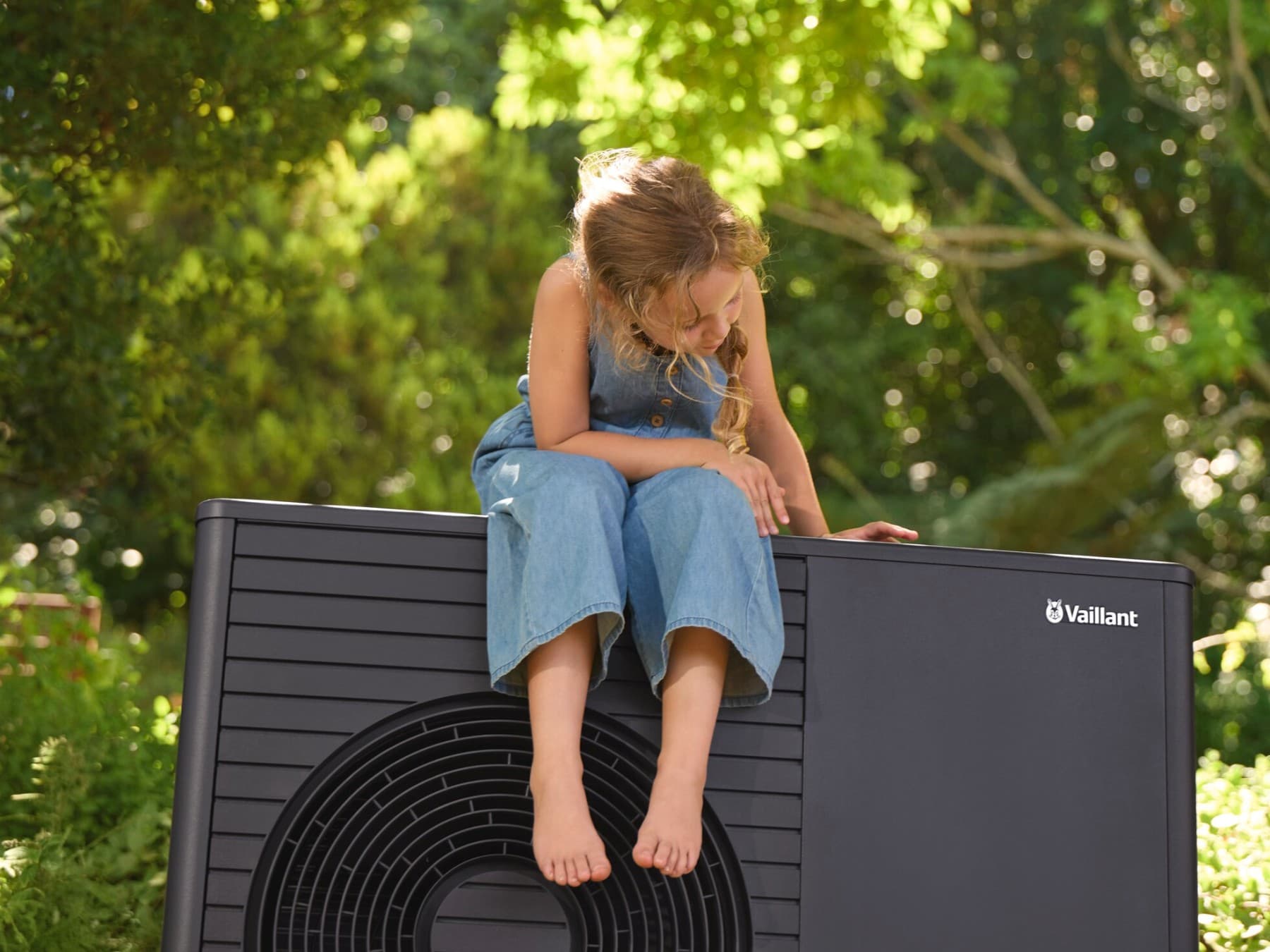 Kind sitzt auf moderner Wärmepumpe von Vaillant