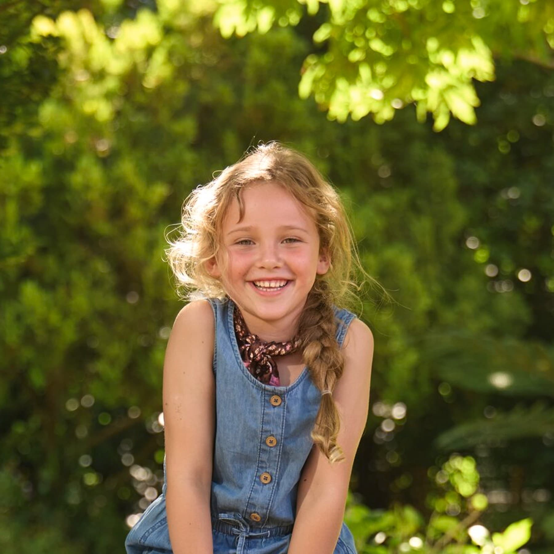 Ein Mädchen sitzt auf einer schwarzgrauen Vaillant Wärmepumpe, die in einem sonnigen Garten steht.