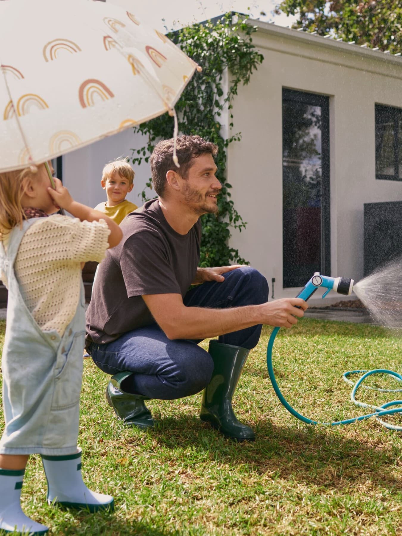Ein Mann beim Rasen wässern mit Kindern im Garten