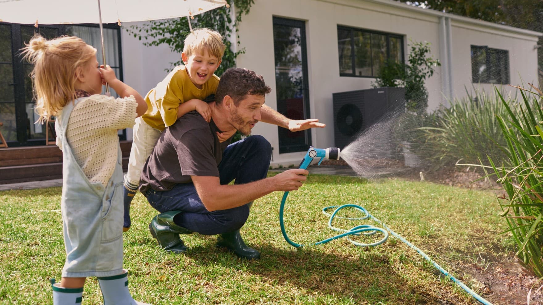 Familie im Garten mit einem Neubau und einer Vaillant Wärmepumpe im Hintergrund