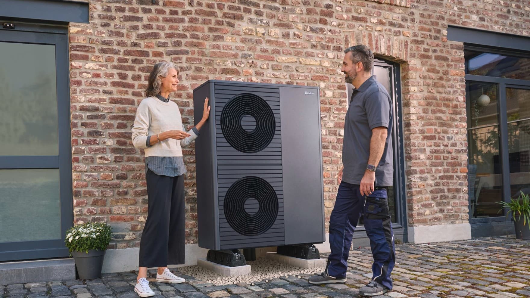 Hausbesitzerin steht mit Fachhandwerker vor Ihrem Haus neben einer Wärmepumpe