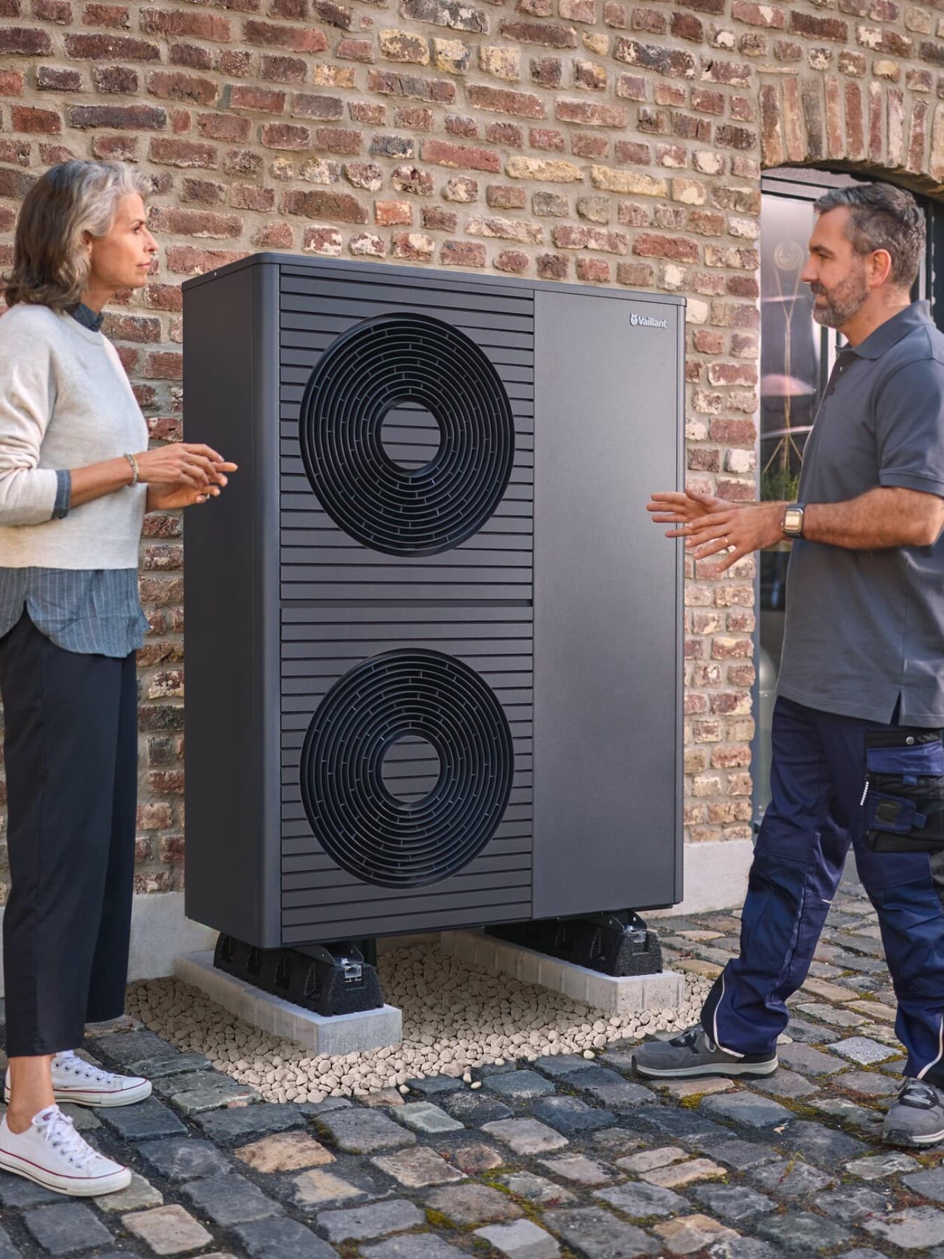 Zwei Vaillant Fachhandwerker gehen sich unterhaltend von einem Haus weg, vor dem eine Vaillant Wärmepumpe steht.