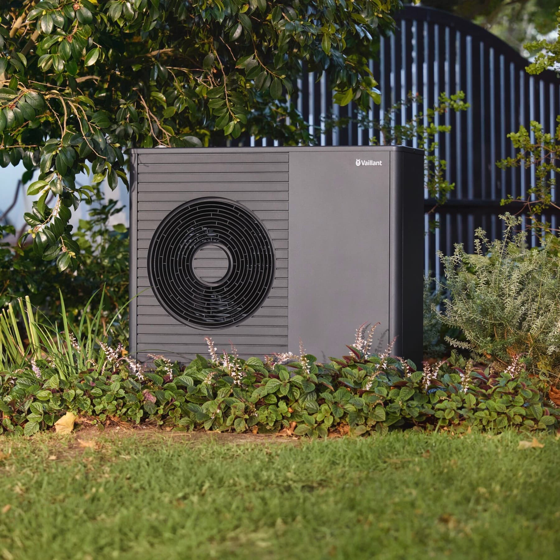 Eine schwarzgraue Vaillant Wärmepumpe steht in einem Garten.