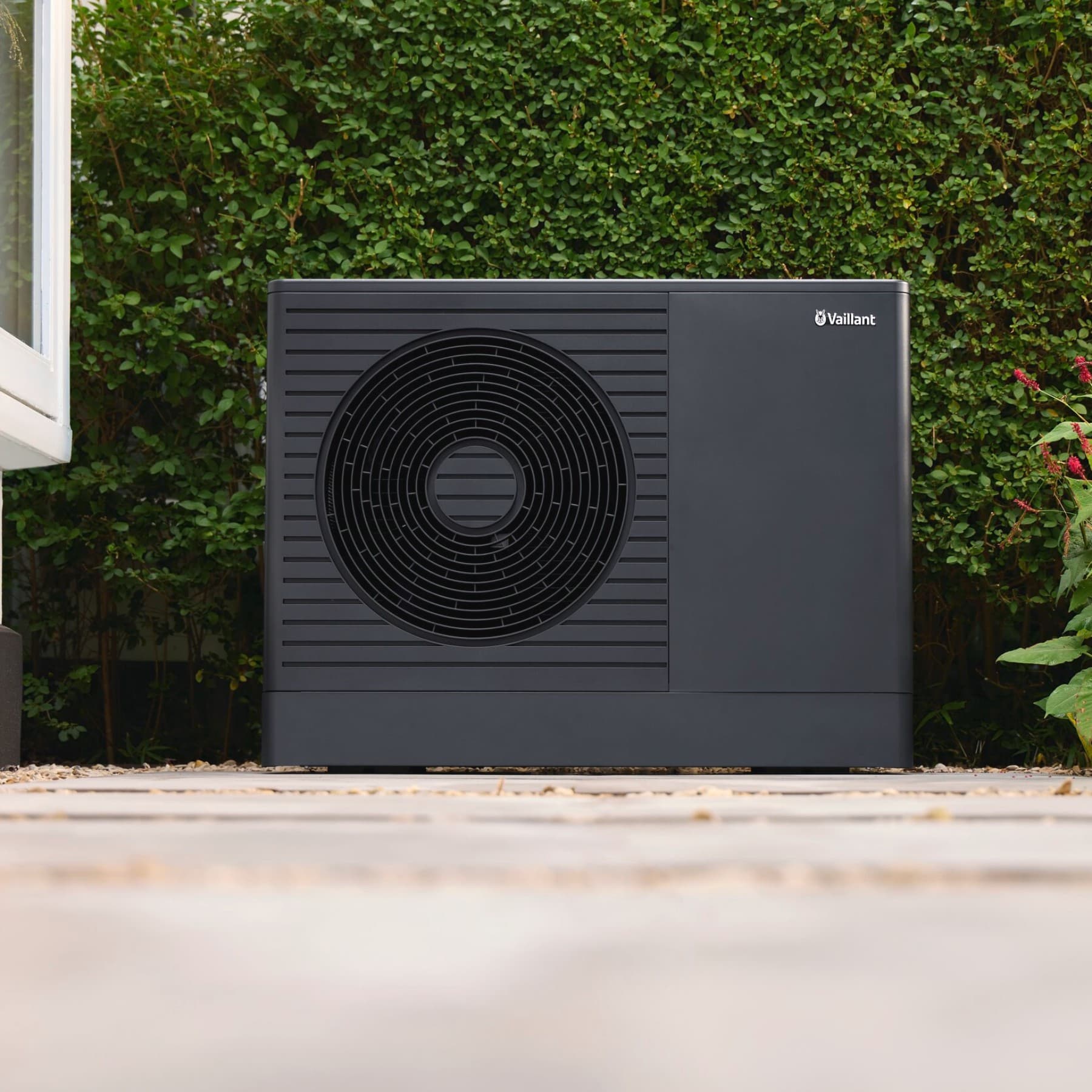 Vaillant Wärmepumpe aroTHERM pro vor einer Hecke vor einem Haus.