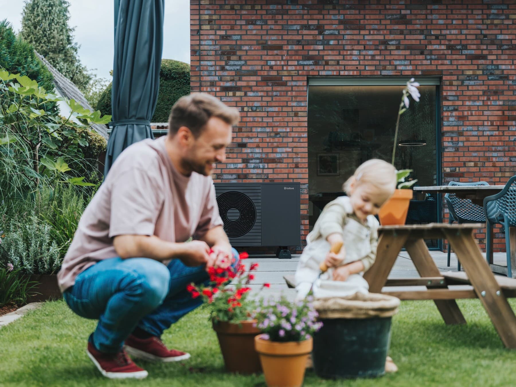 Mann mit seinem Kind im Garten am Spielen. Im Hintergrund ist eine Vaillant Wärmepumpe zu sehen.