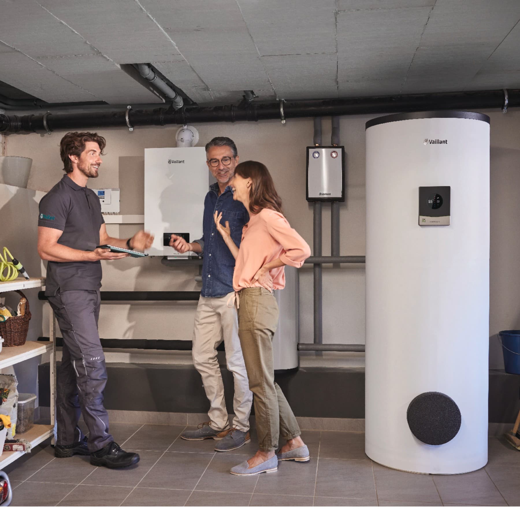 Ein Mann und eine Frau stehen mit einem Vaillant Techniker in einem Heizungskeller vor einem Vaillant Heizsystem.