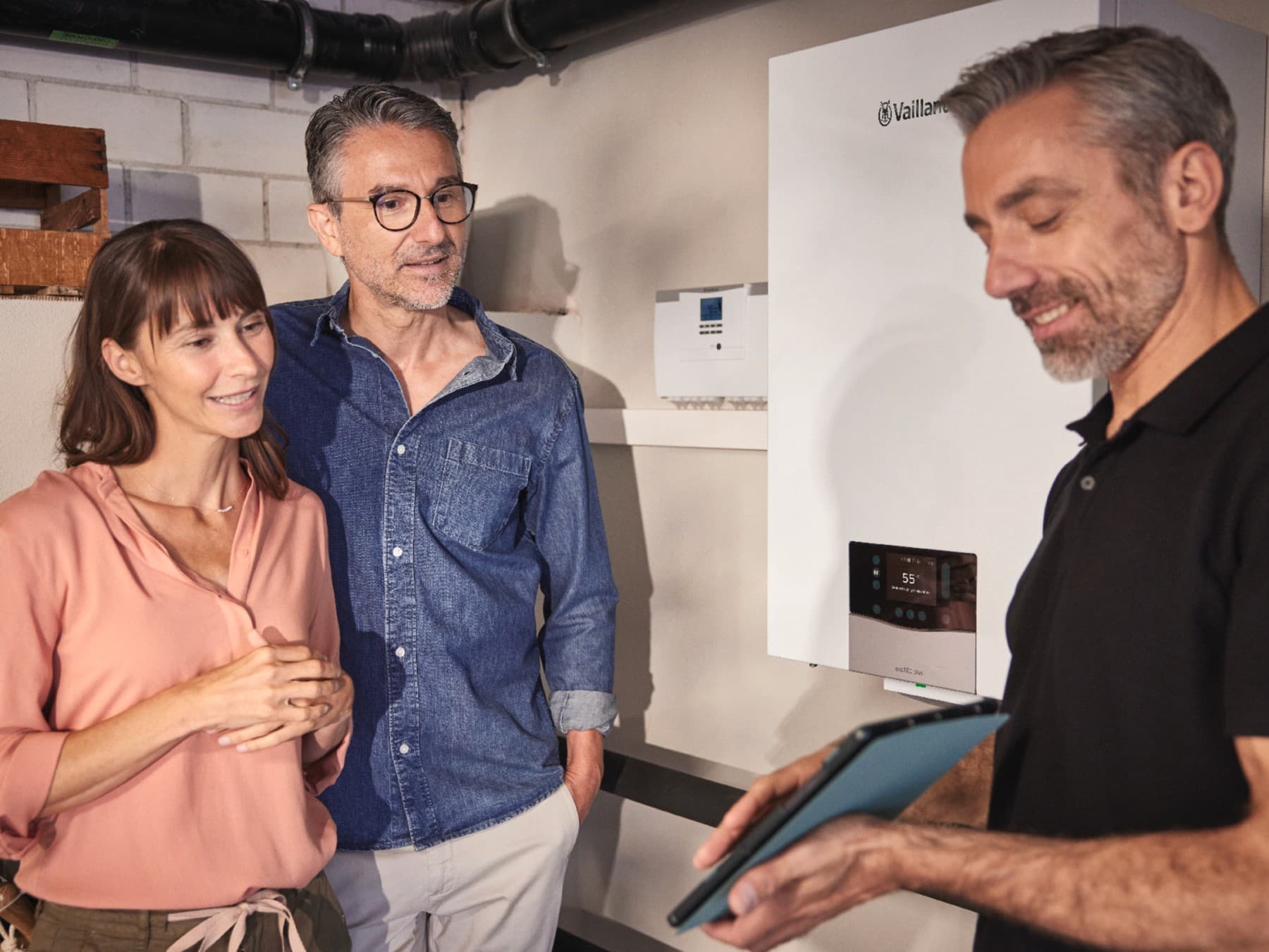 Ein Ehepaar moit einem Fachhandwerker im Keller vor einer Hybridheizung