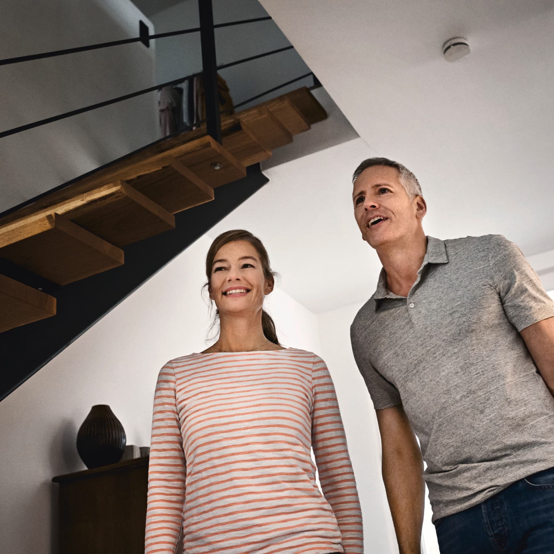 Zwei Personen stehen in einem Flur neben einer Treppe in einem Einfamilienhaus.