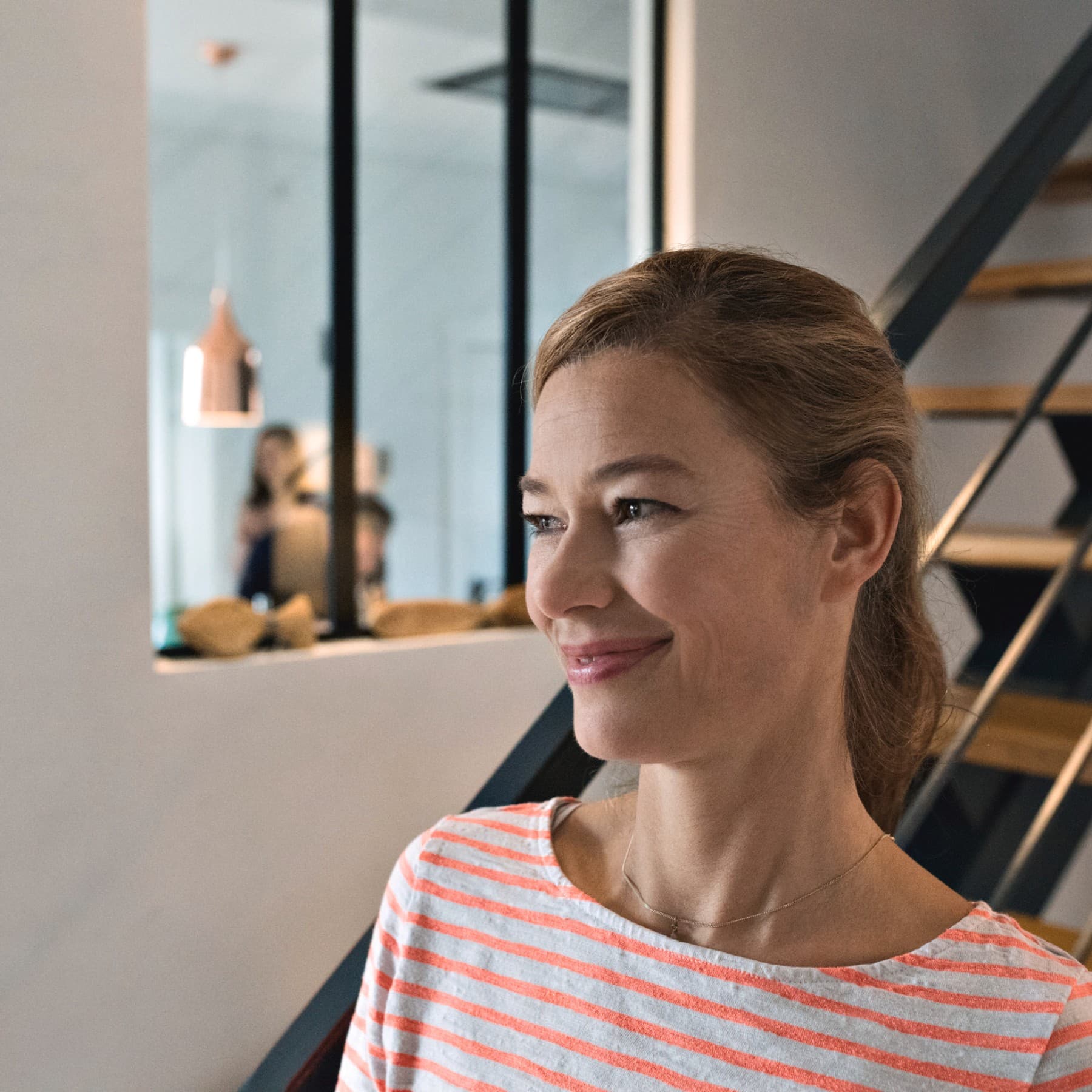 Eine Frau steht lächelnd vor einer Treppe in einem Einfamilienhaus.