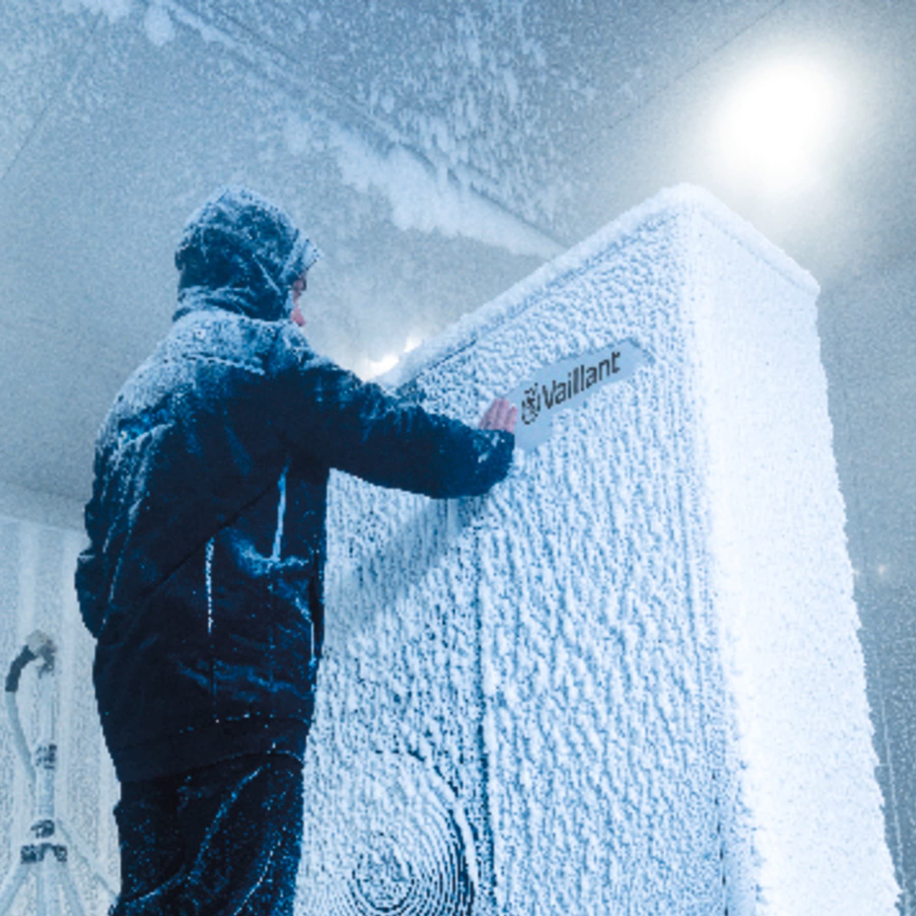 Eine Vaillant Wärmepumpe steht in einem kalten Testraum, in dem es schneit und friert. Ein Mitarbeiter steht davor und entfernt den Schnee vom Vaillant Logo.