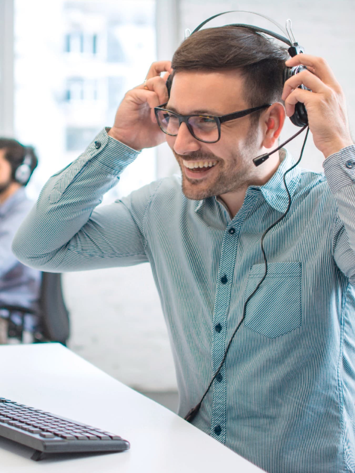 Ein Mann sitzt vor einem Computer und setzt sich lächelnd ein Headset auf.