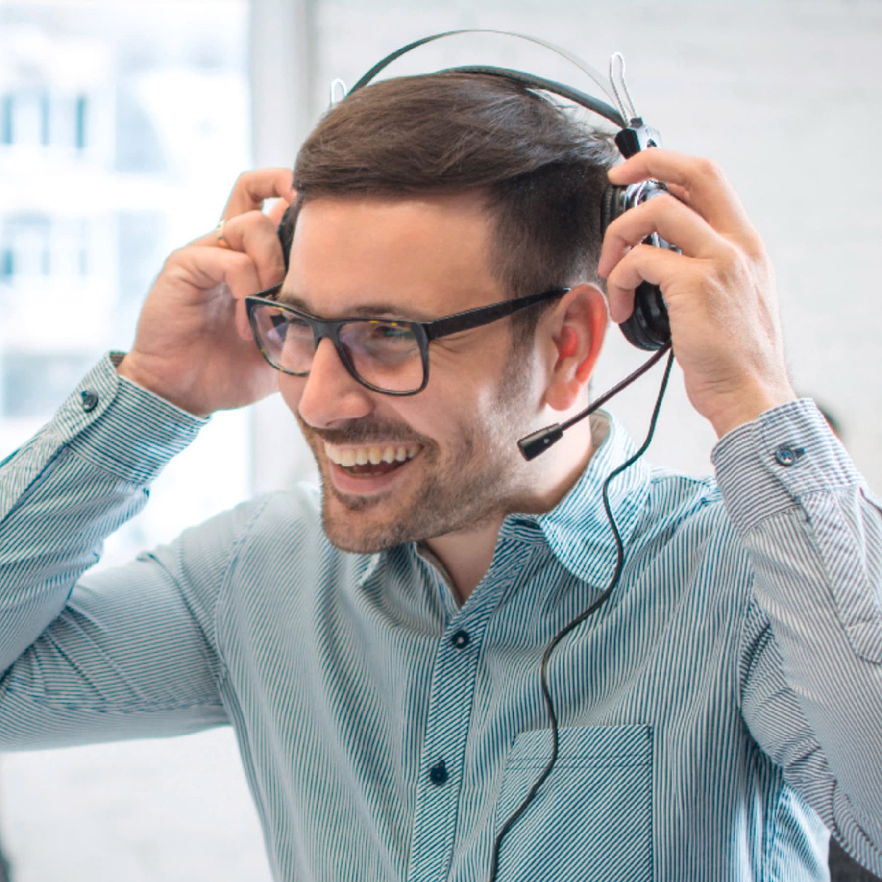 Ein Mann sitzt vor einem Computer und setzt sich lächelnd ein Headset auf.